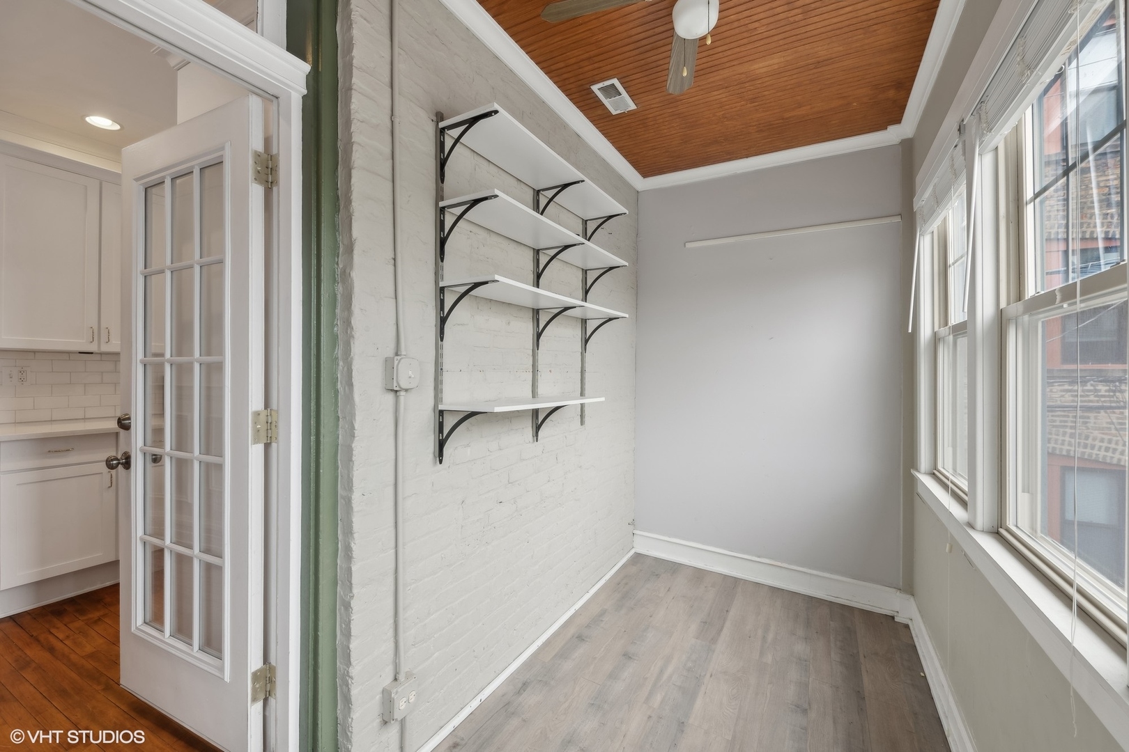 Narrow room with white brick shelving, a wood-paneled ceiling, and tall windows.