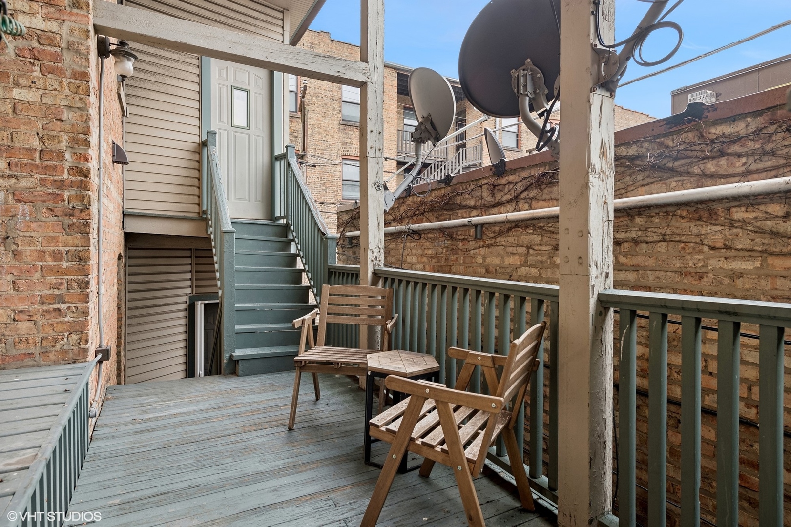 Wooden courtyard deck with seating, green railings, and stairs leading to a white door.