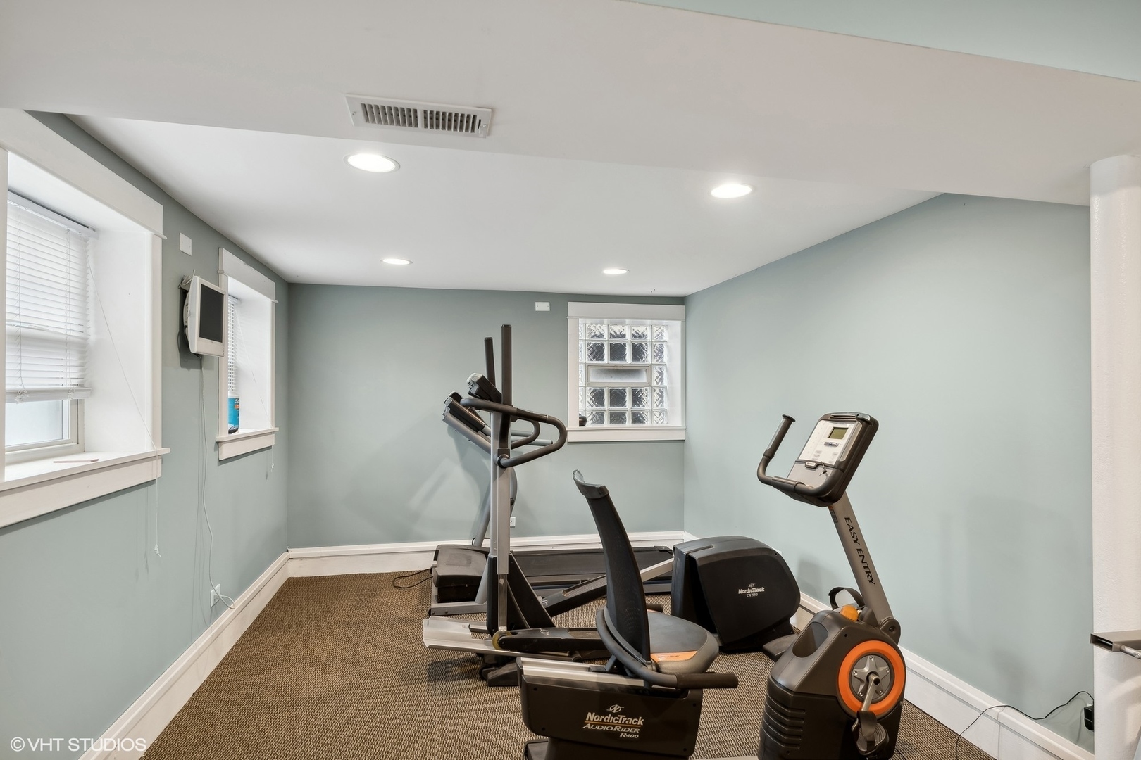 Home gym with NordicTrack exercise equipment, pale blue-green walls, and a glass-block window.