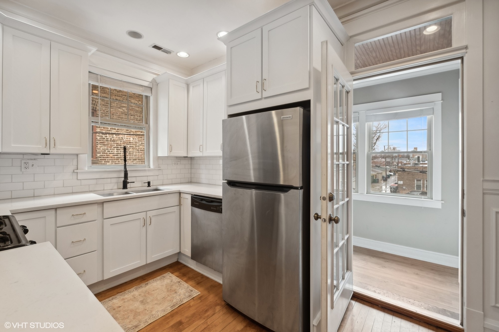 White kitchen with subway tile, stainless-steel appliances, and a glass-paneled door to a bright adjoining room.