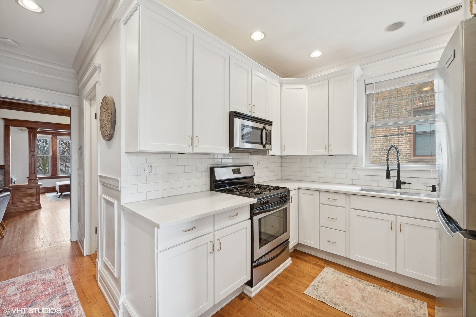 Bright kitchen with white cabinetry, subway tile backsplash, stainless steel appliances, and hardwood floors.