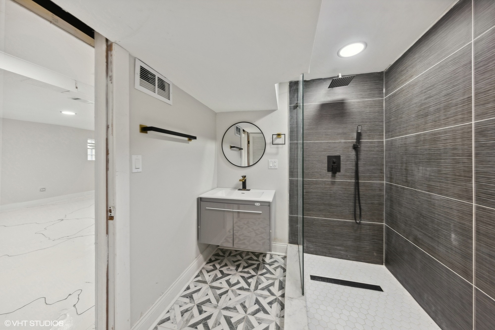 Modern bathroom with a geometric tile floor and glass-enclosed shower.