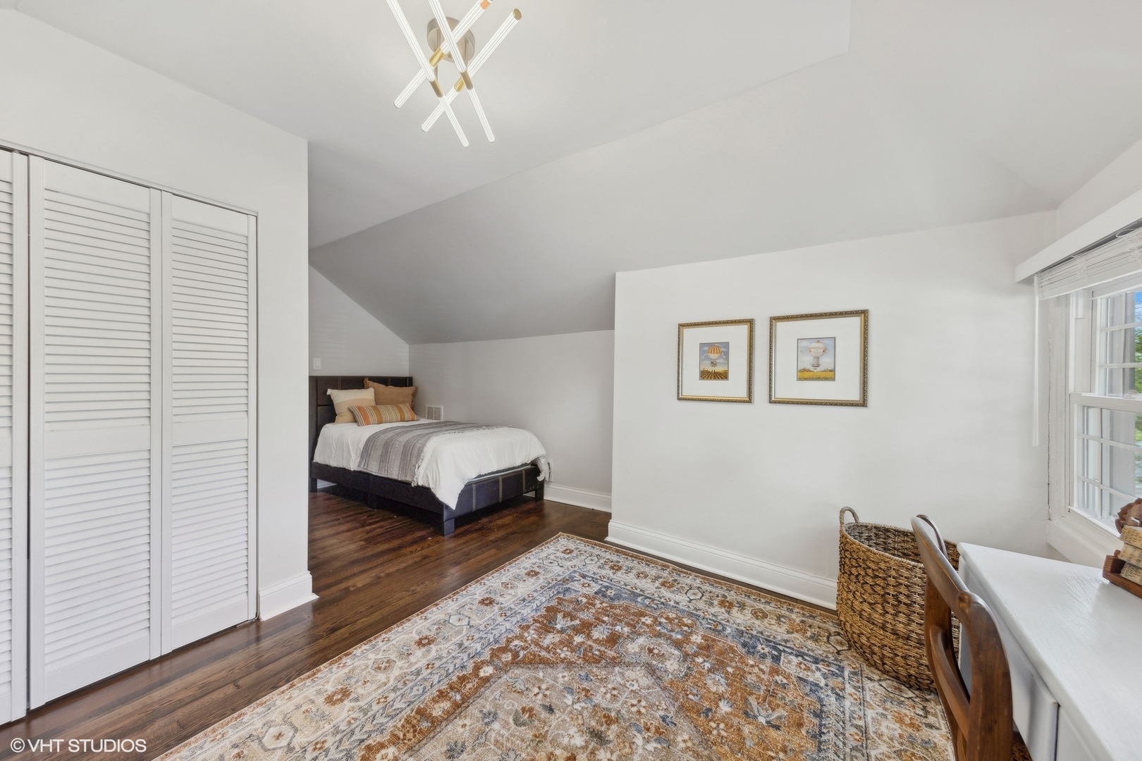 Bedroom with a bed in a sloped-ceiling alcove, hardwood floors, and white louvered closet doors.