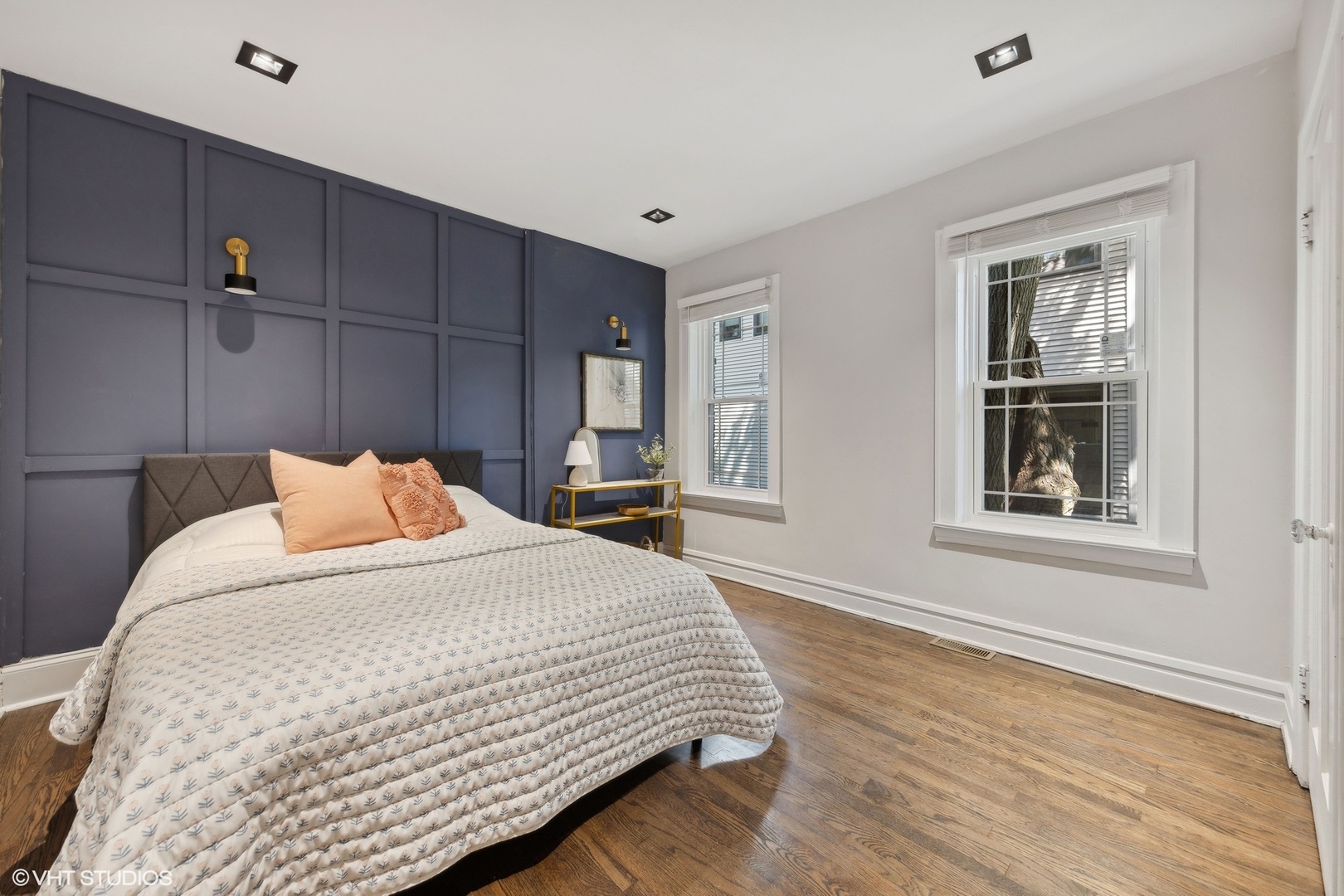 Staged bedroom with a dark blue paneled accent wall, peach pillows, and hardwood floors.