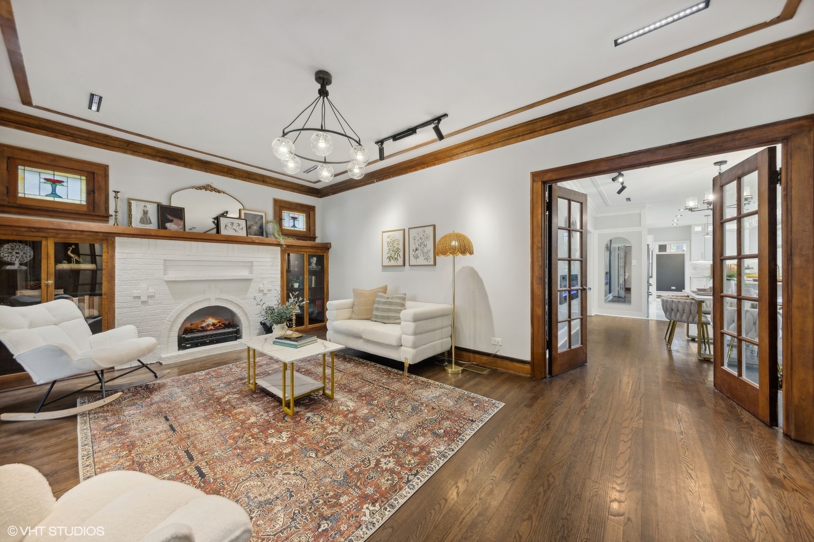 Living room with a white brick fireplace, wood built-ins, French doors, and a patterned rug.