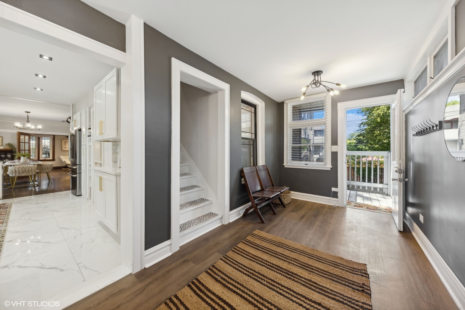 Entry foyer with a striped rug and staircase, opening to a bright kitchen and dining area.