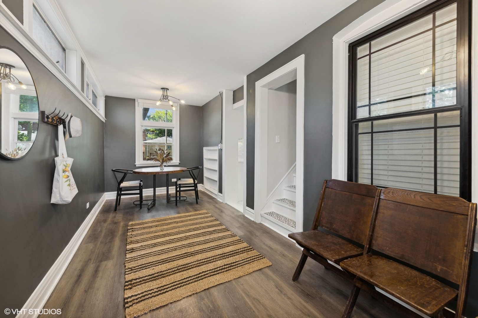 Furnished entryway with a wooden bench, wall hooks, striped rug, and staircase doorway.