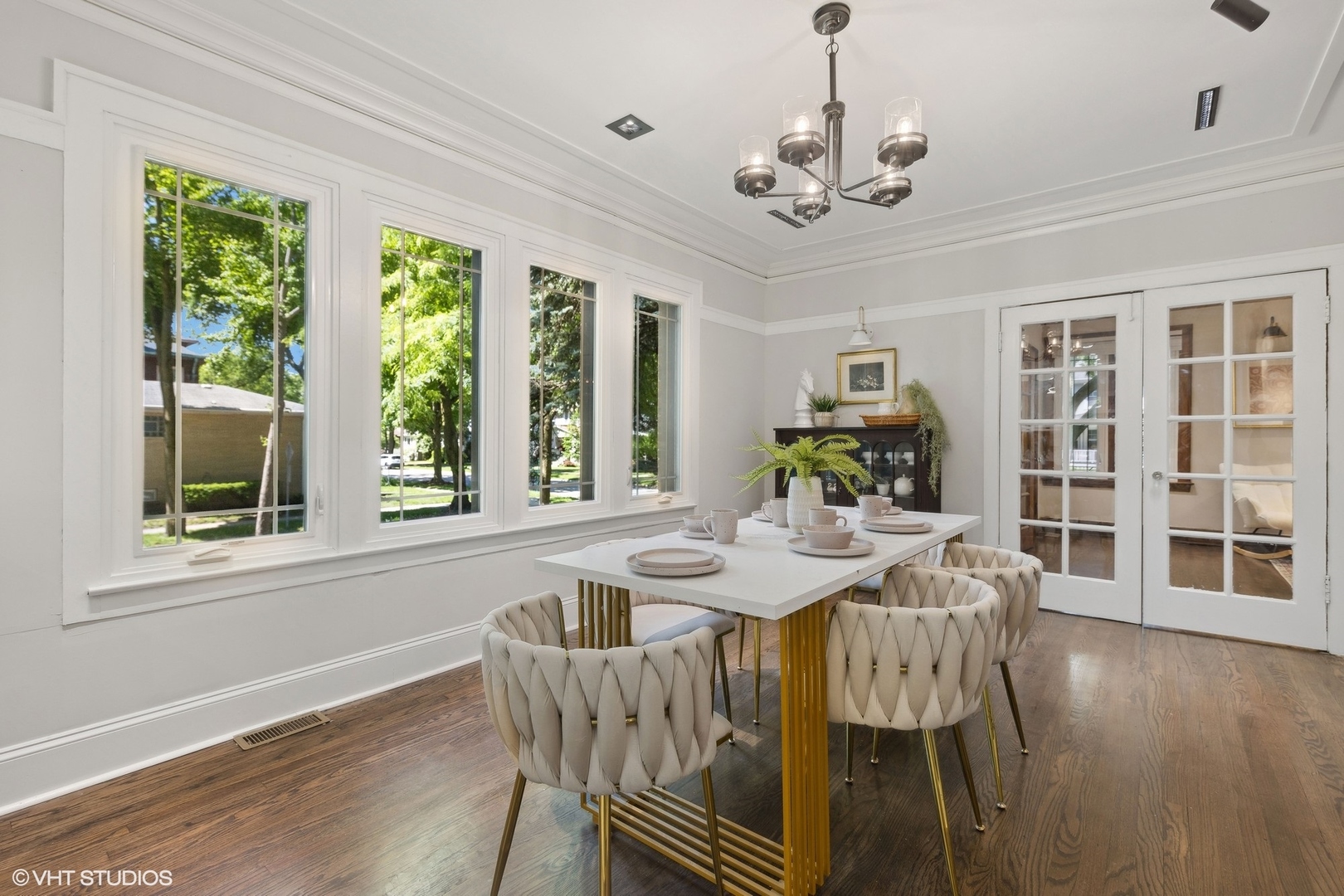 Dining room with tall windows, a white table, upholstered chairs, and hardwood floors.