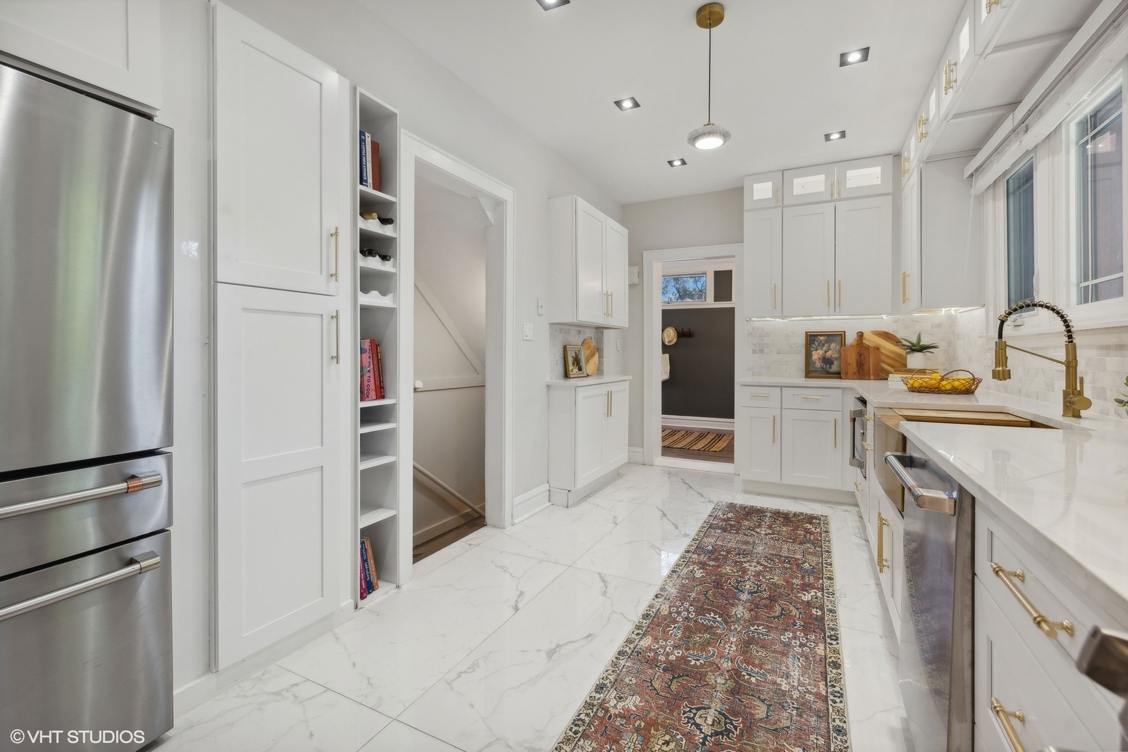White kitchen with marble-look flooring, stainless appliances, brass hardware, and a patterned runner.