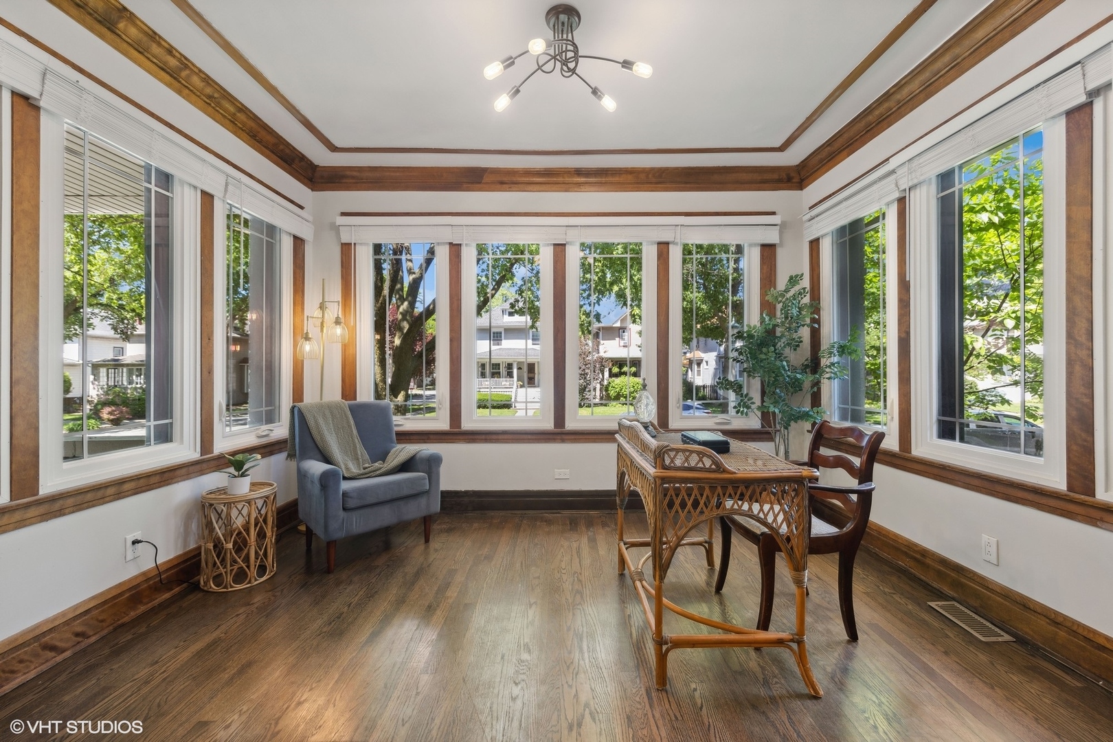 Sunroom with wood-trimmed windows, hardwood floors, and wicker furniture.
