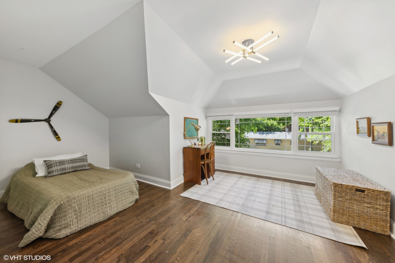 Bedroom with a sloped ceiling, wide windows, dark wood floors, and a bed.