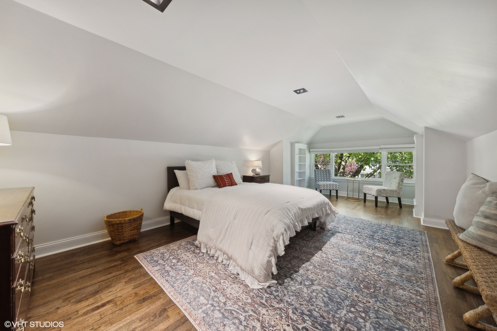 Attic bedroom with a white bed, patterned rug, and window-side sitting area.