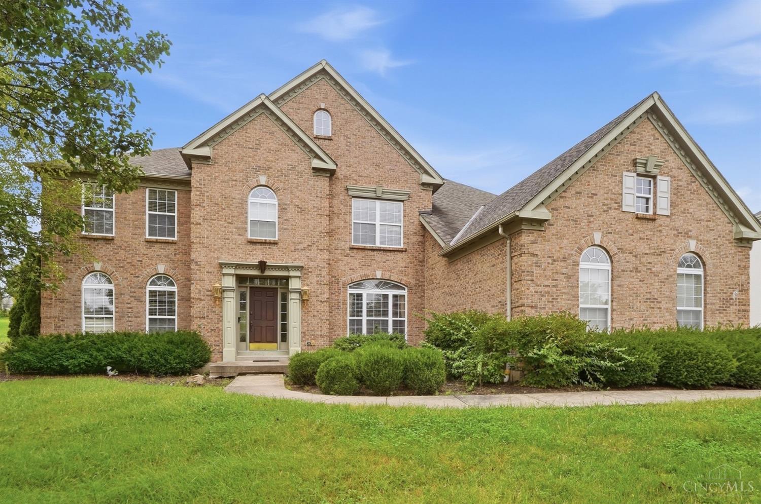 Two-story brick house with arched windows, gabled rooflines, and a landscaped front lawn.
