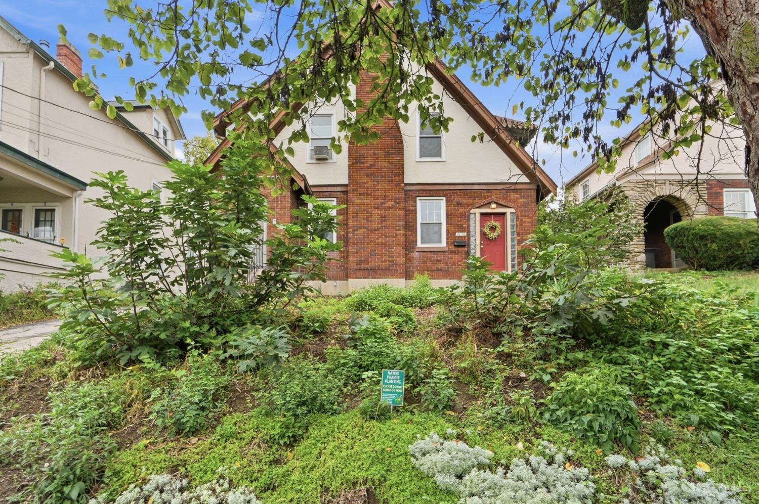 Brick-and-cream house with a red front door behind a lush native prairie garden.