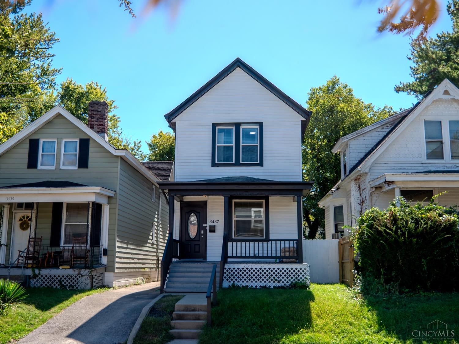 White two-story house with dark trim, a covered porch, and front steps between neighboring homes.