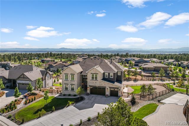 Aerial view of a two-story home with a three-car garage, landscaped yard, and mountain range beyond the neighborhood.