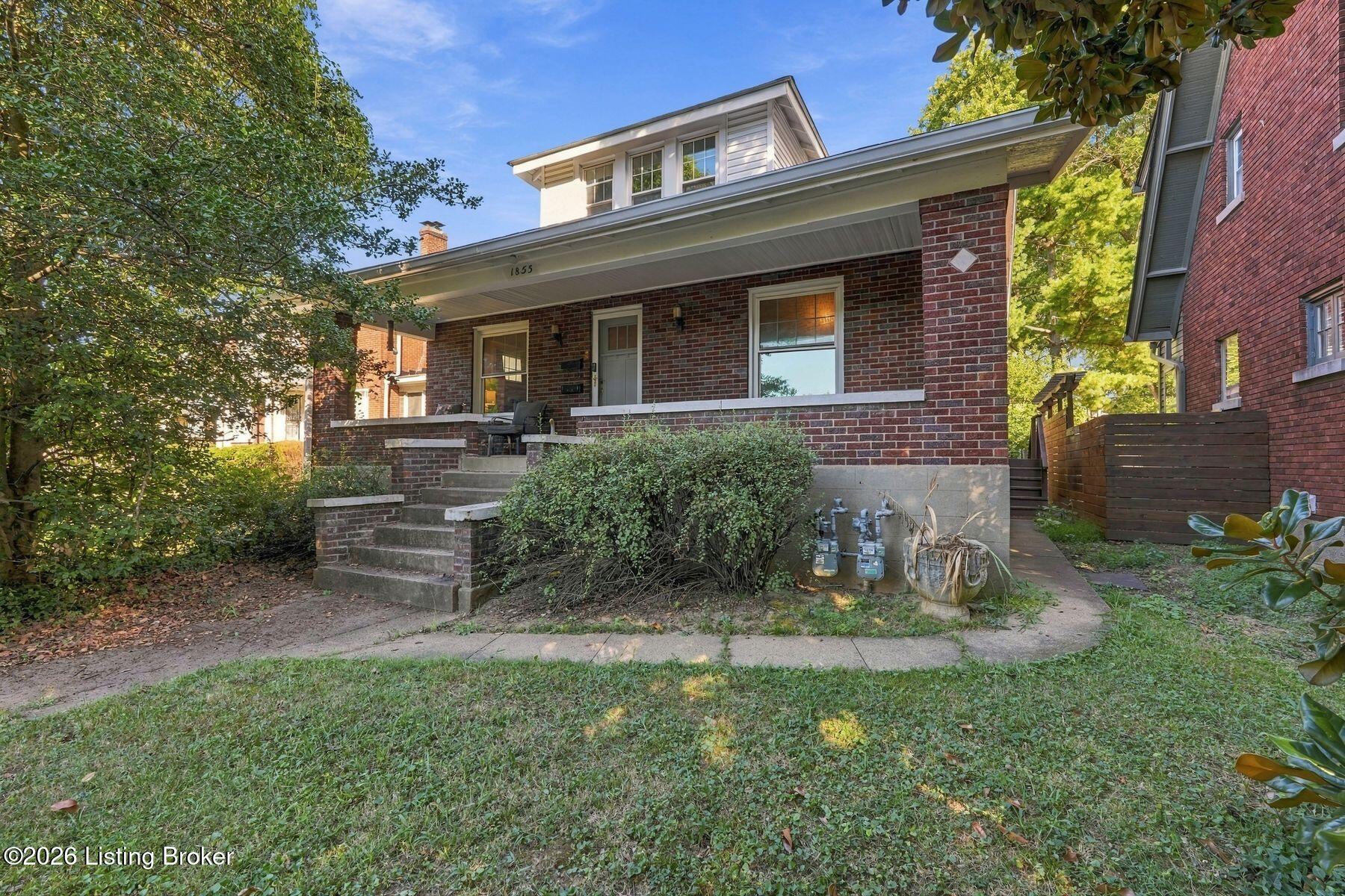 Brick two-story house with a covered porch, broad front steps, and mature trees.