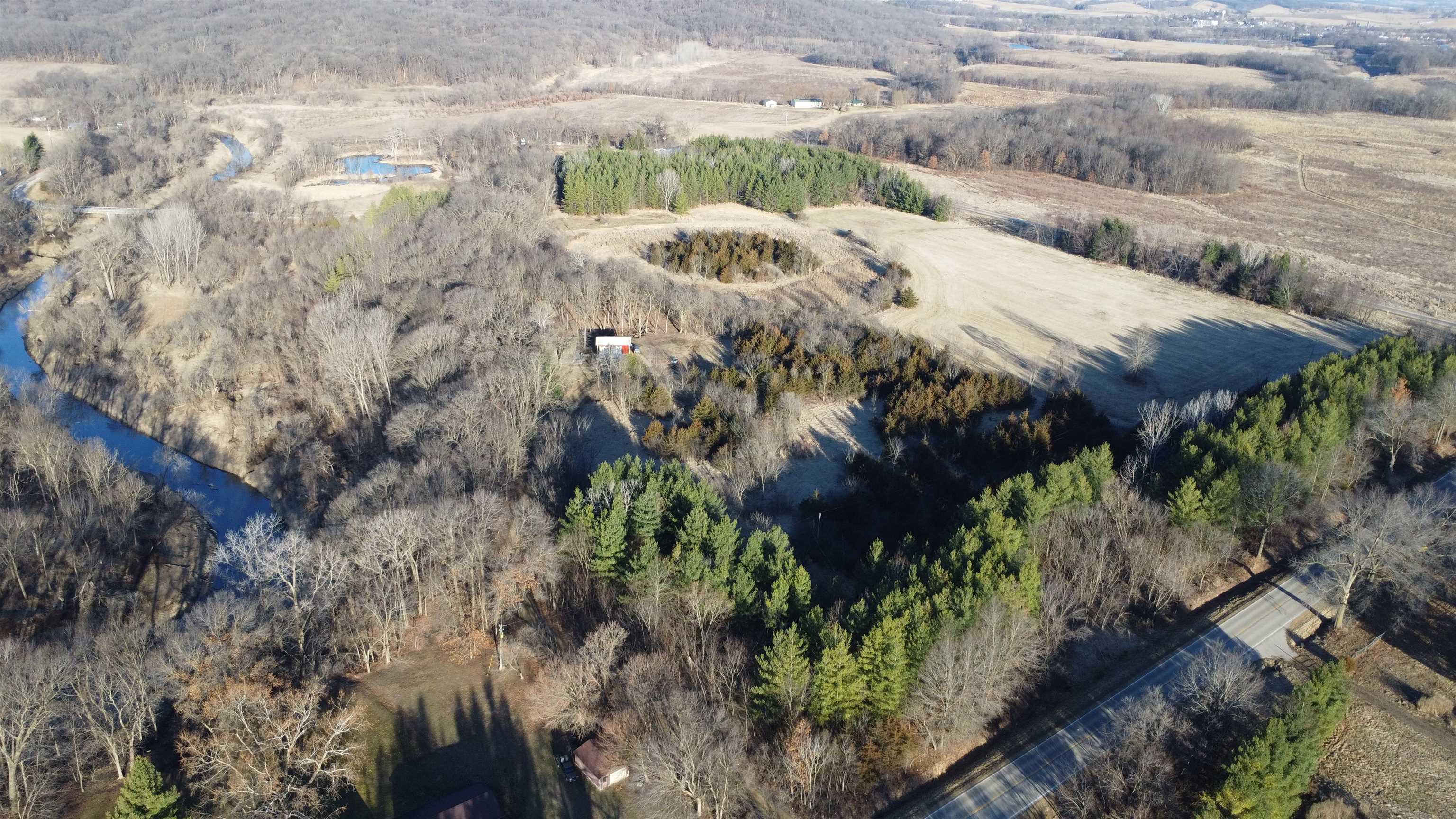 Aerial view of wooded land with a winding creek, open fields, and a road along its edge.