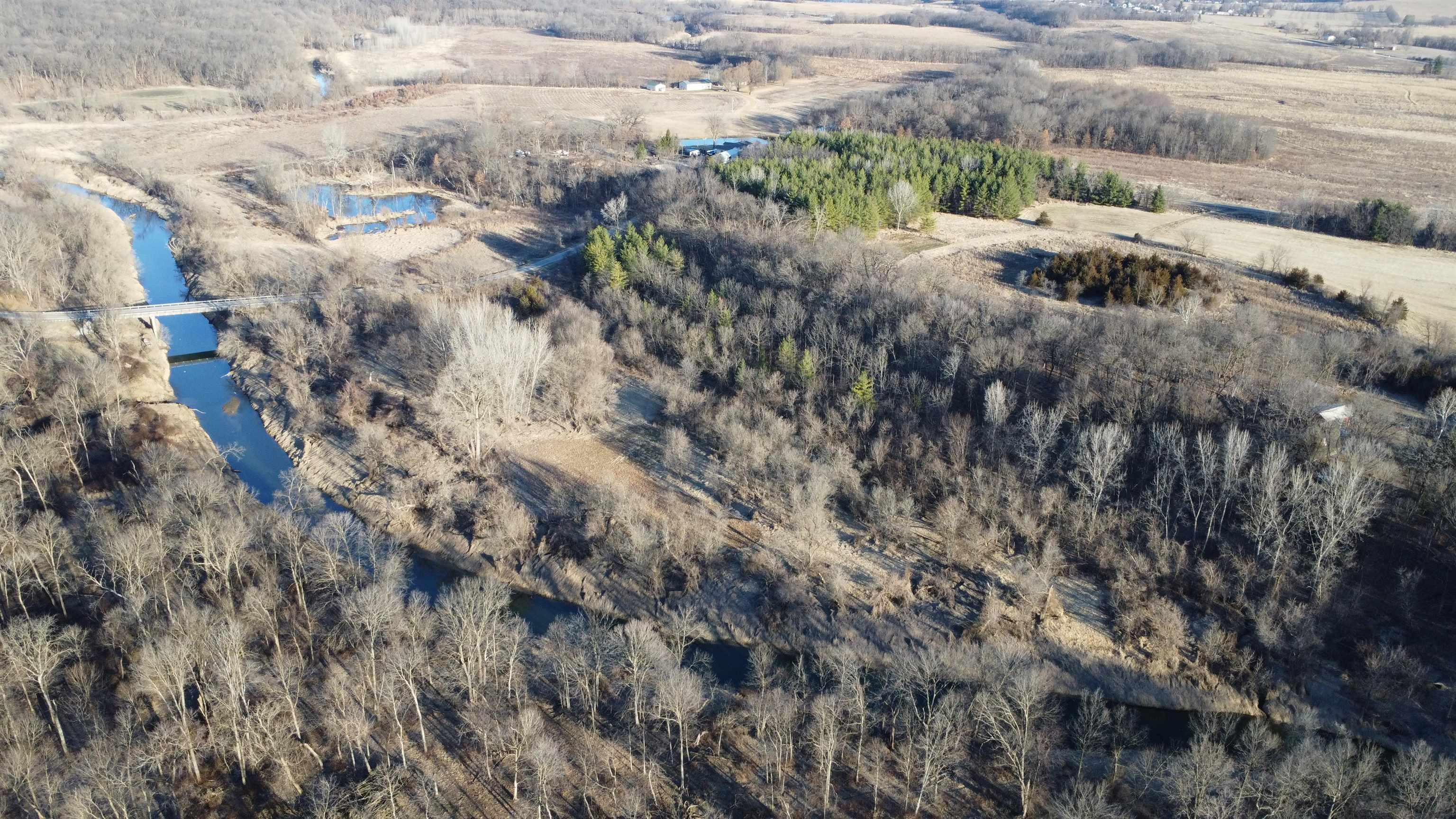 Aerial view of wooded land with a creek, small ponds, and a bridge.