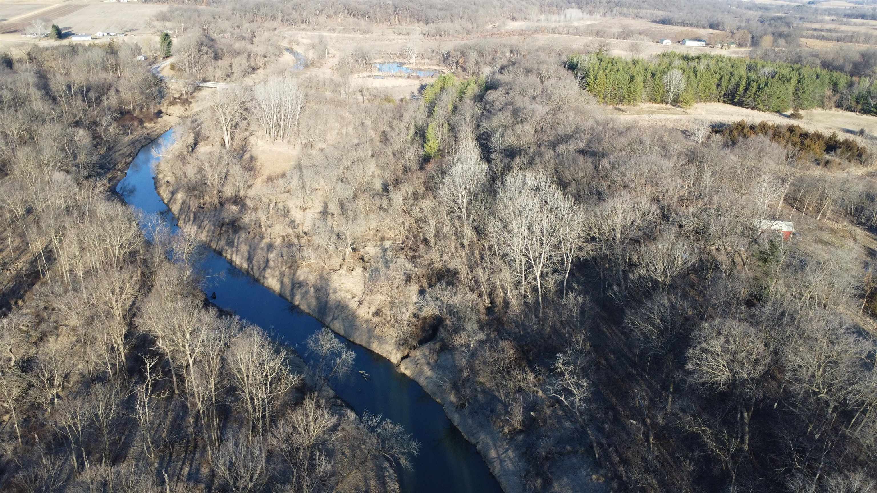 Aerial view of wooded land with a winding creek and open fields.