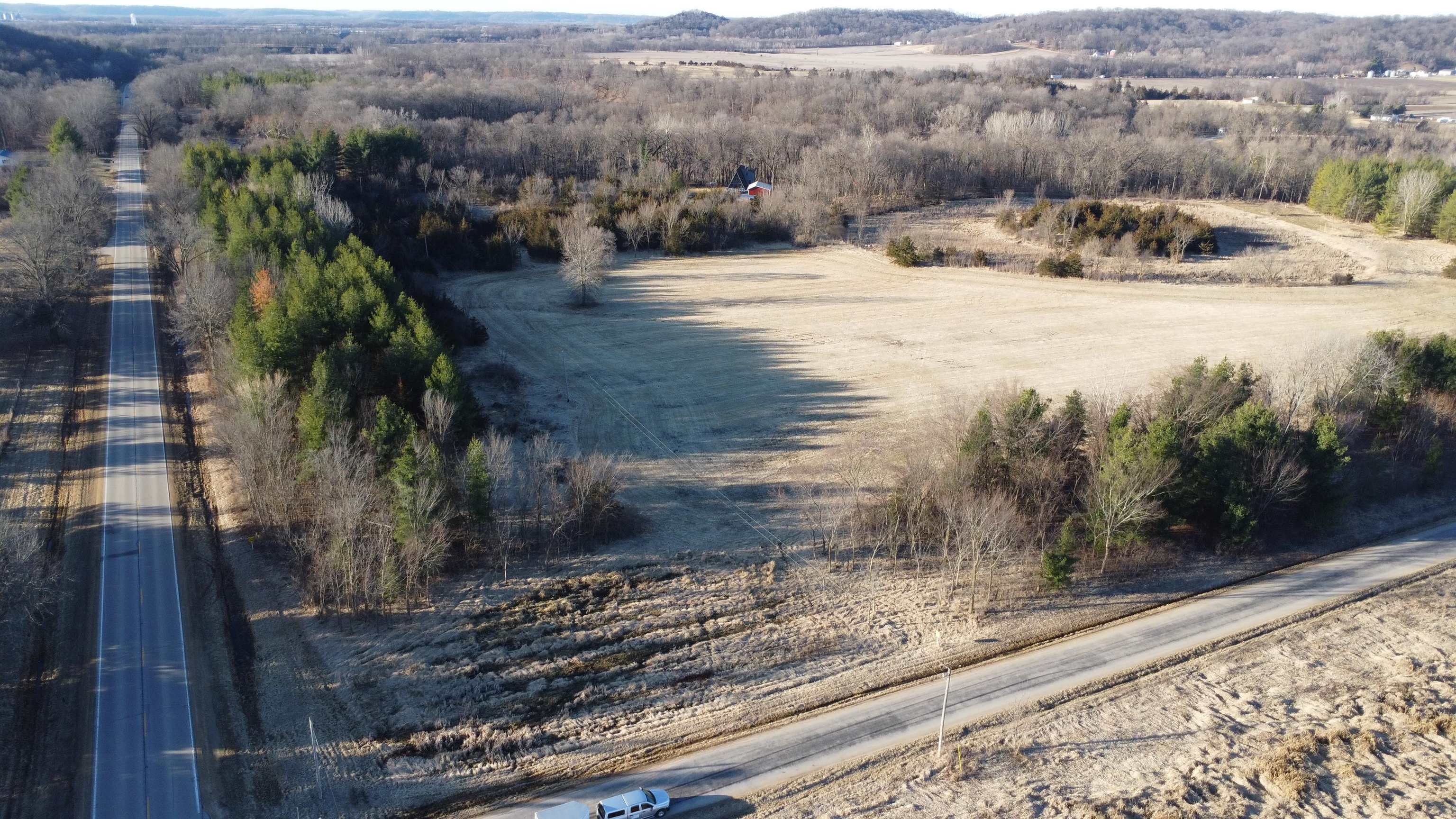 Aerial view of open rural land bordered by woods and roads.