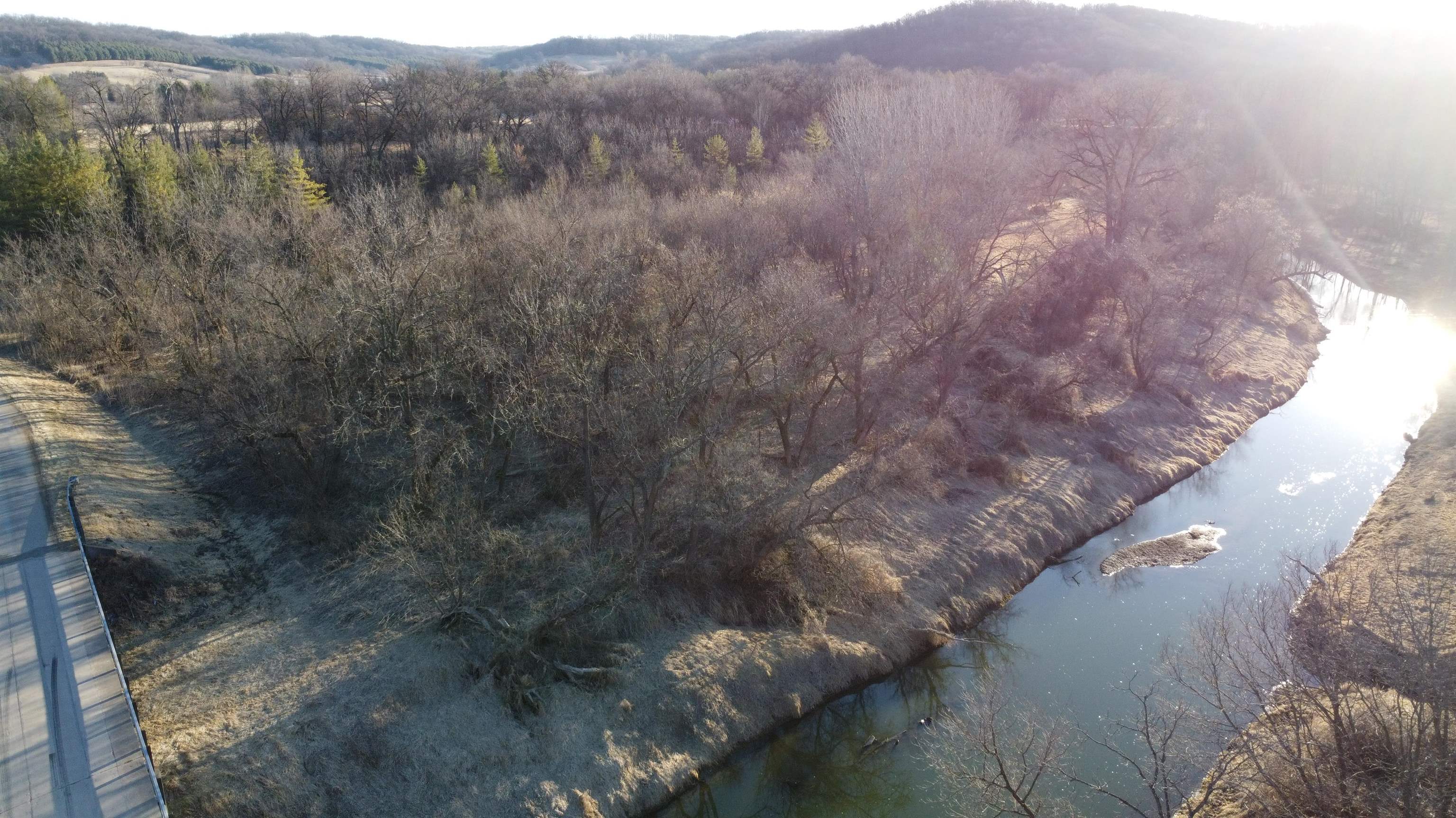 Aerial view of wooded land beside a winding river, with a road along the edge.