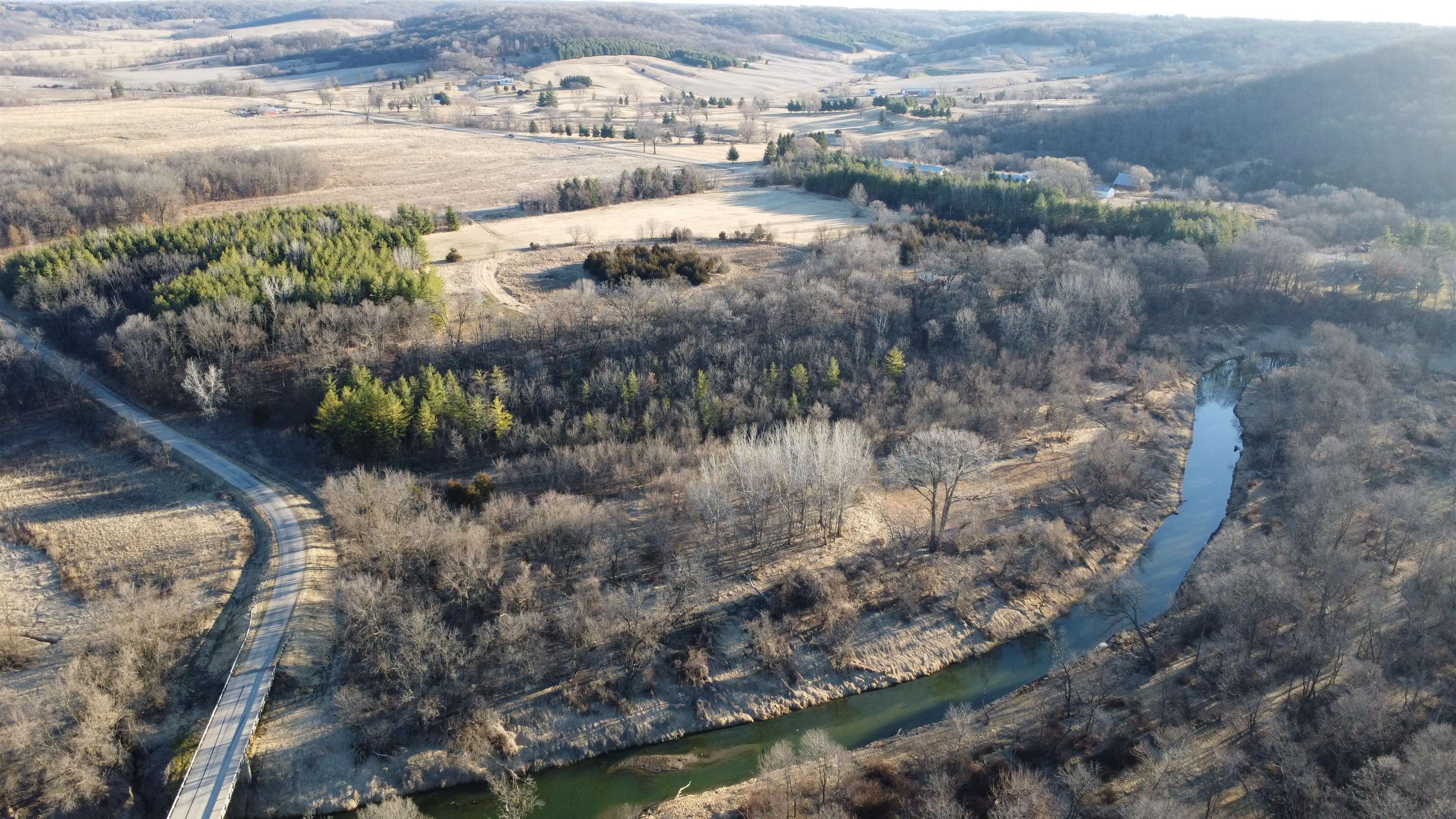 Aerial view of wooded acreage with a winding creek and road bridge.