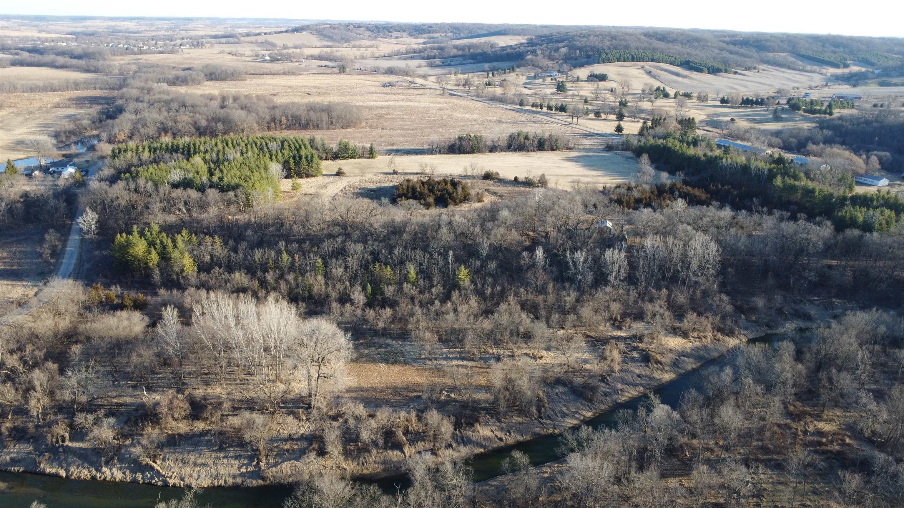 Aerial view of wooded acreage with open fields and a winding creek.