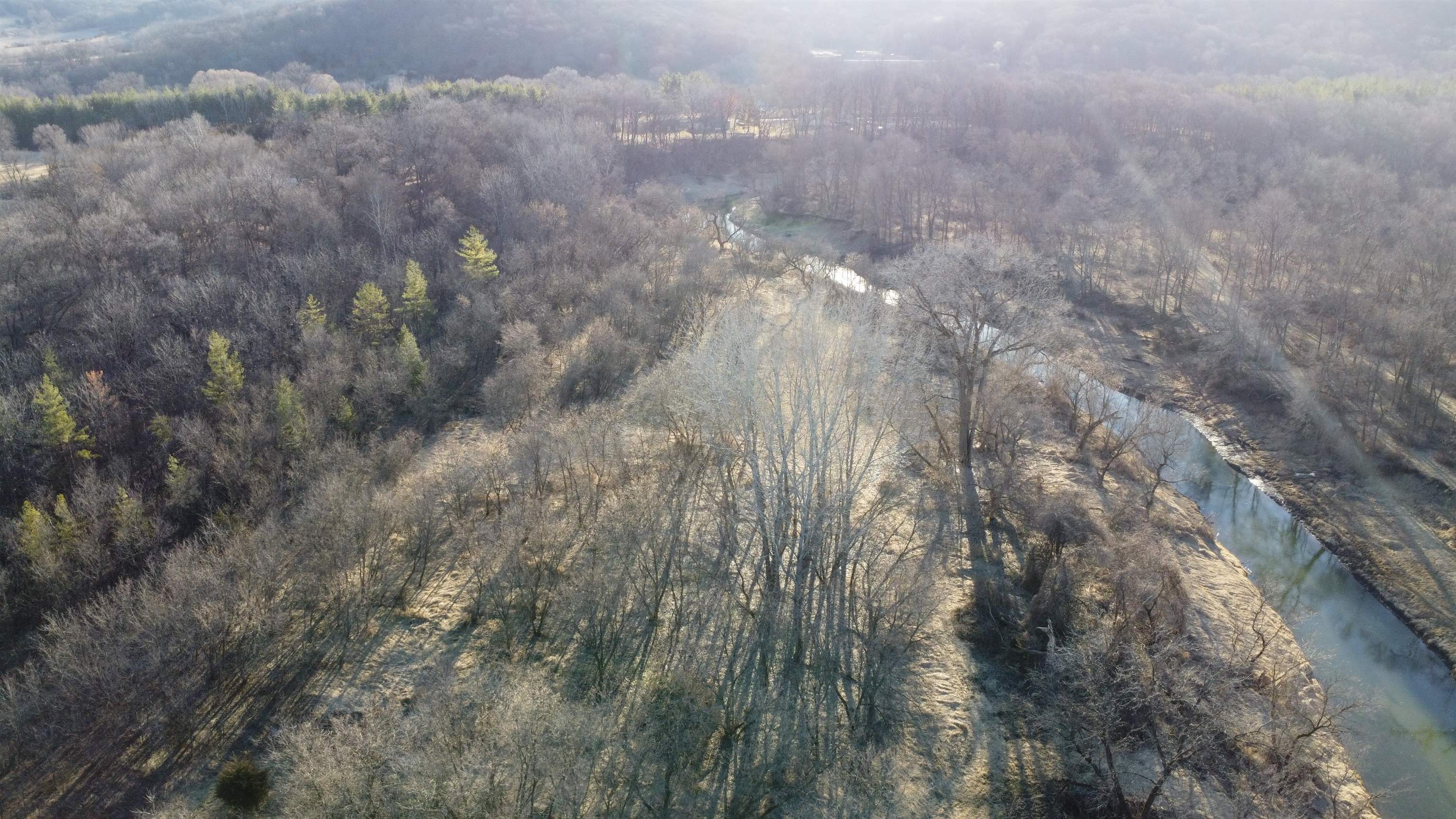 Aerial view of wooded land with a winding creek and open grassy clearing.