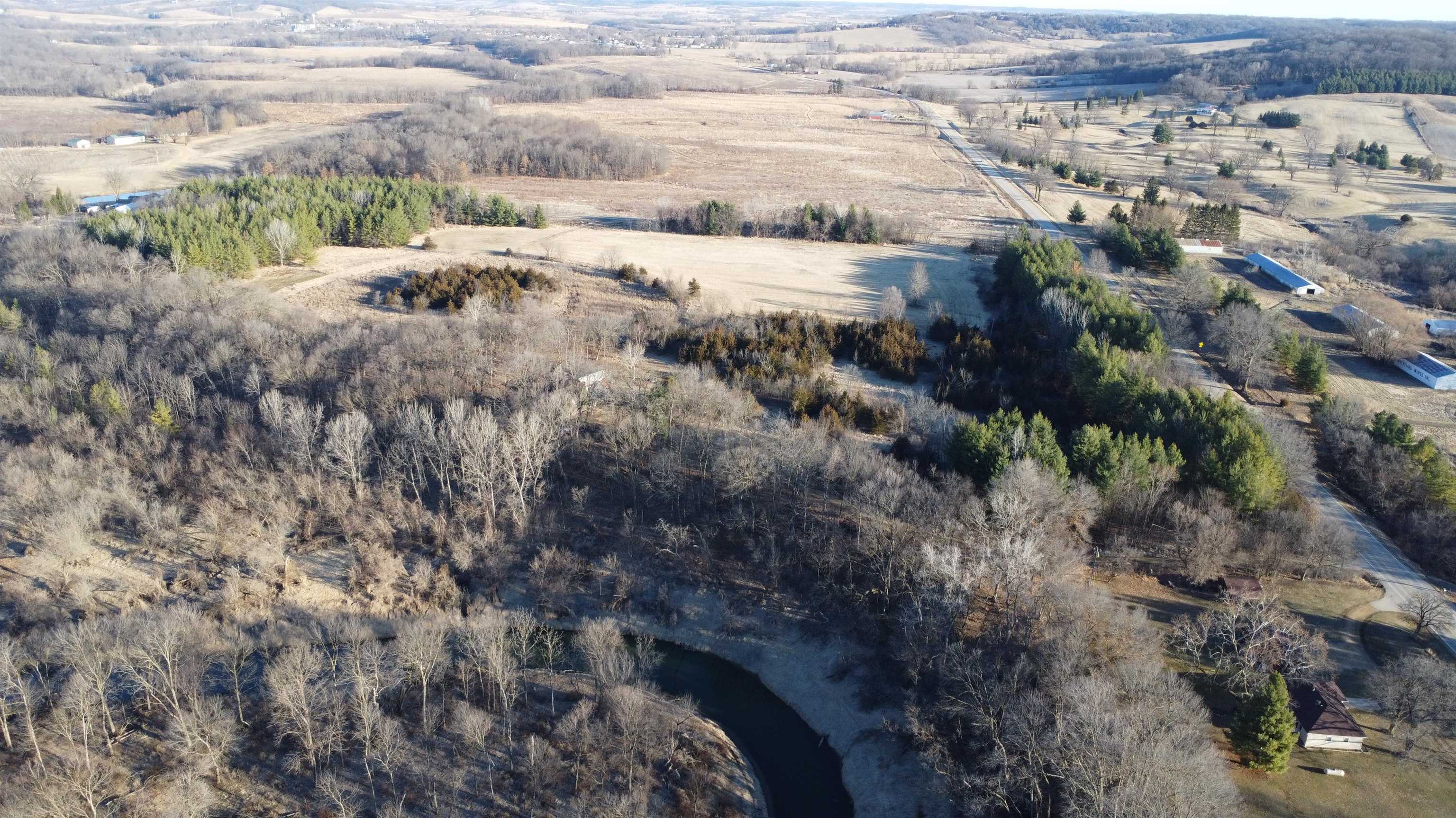 Aerial view of wooded land with a winding river, open fields, and a nearby road.