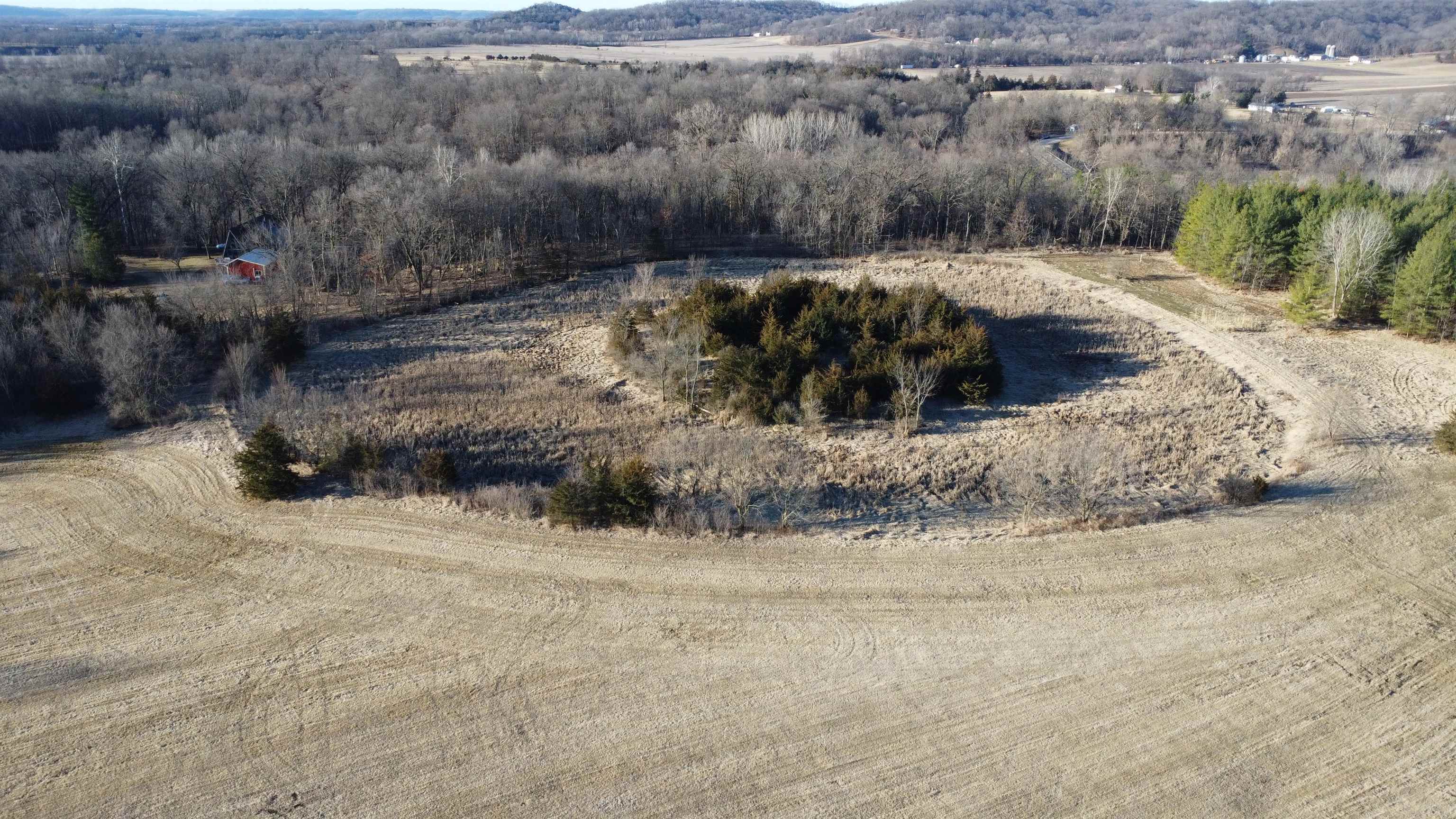 Aerial view of wooded acreage with open fields and a small red outbuilding.
