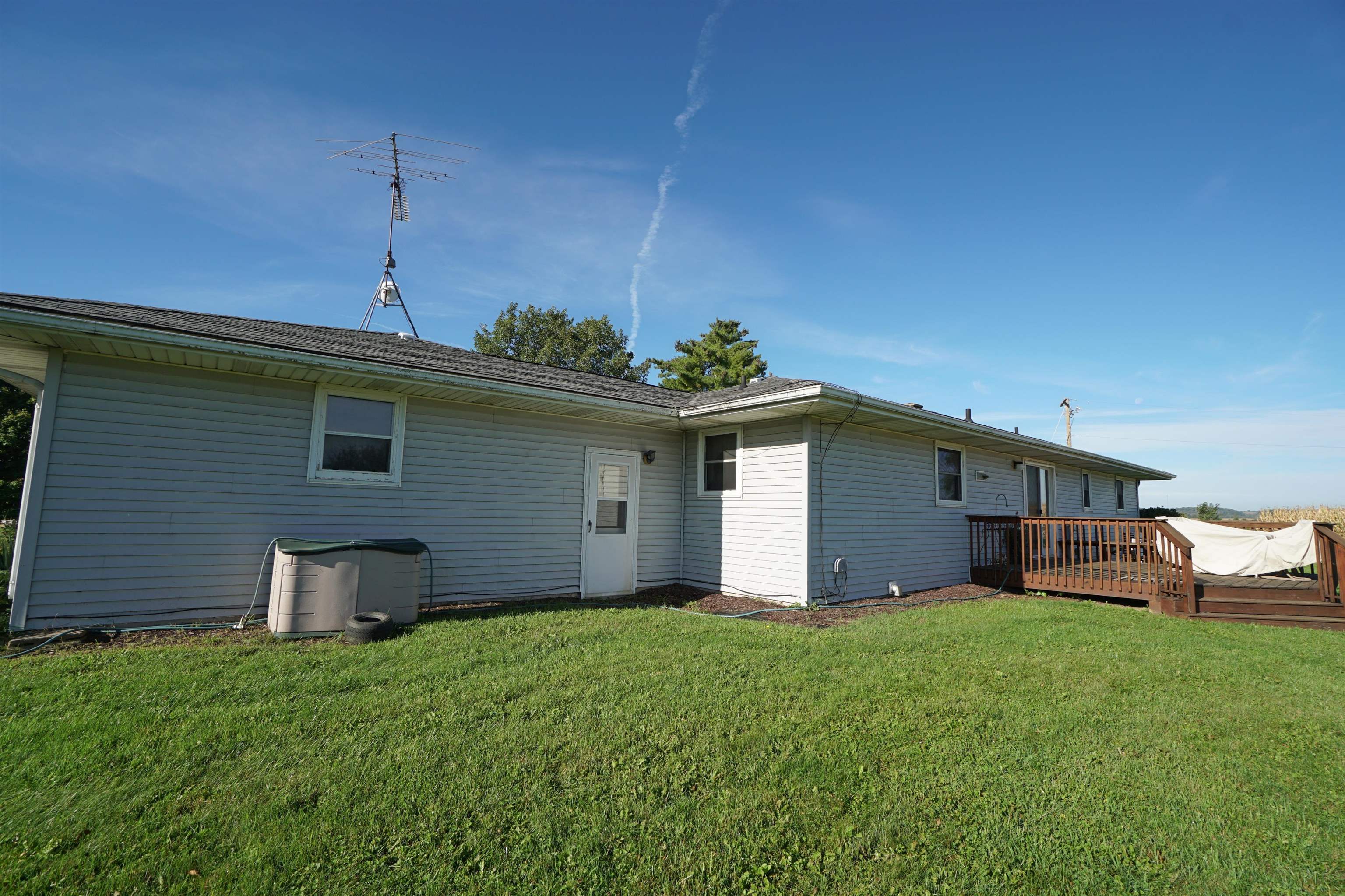 Rear of a single-story gray-sided home with a wooden deck, rooftop antenna, and wide lawn.