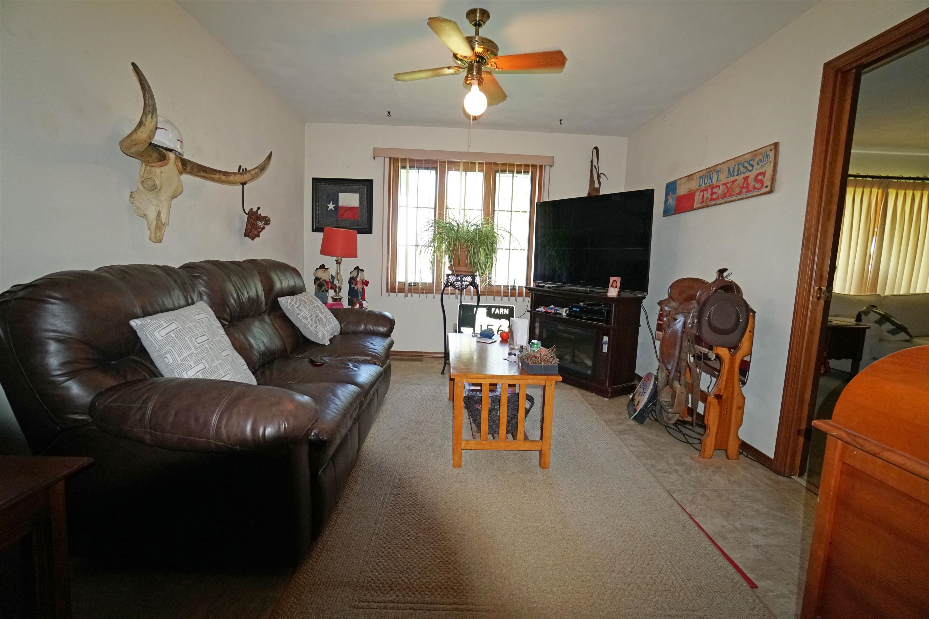Living room with a leather sectional, TV fireplace, longhorn skull, and Western saddle display.