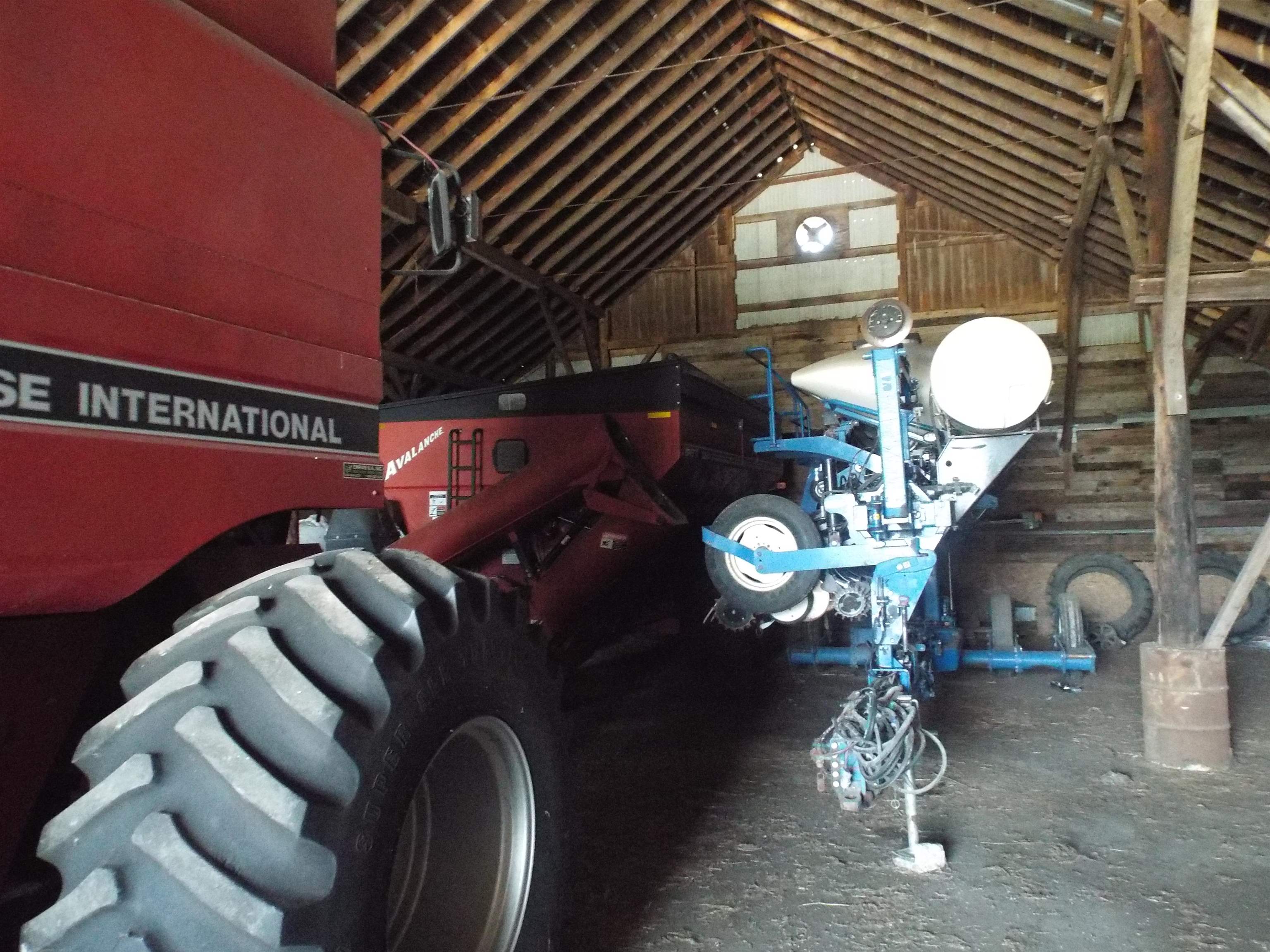 Farm machinery inside a timber-framed barn, including a red International tractor and blue equipment.