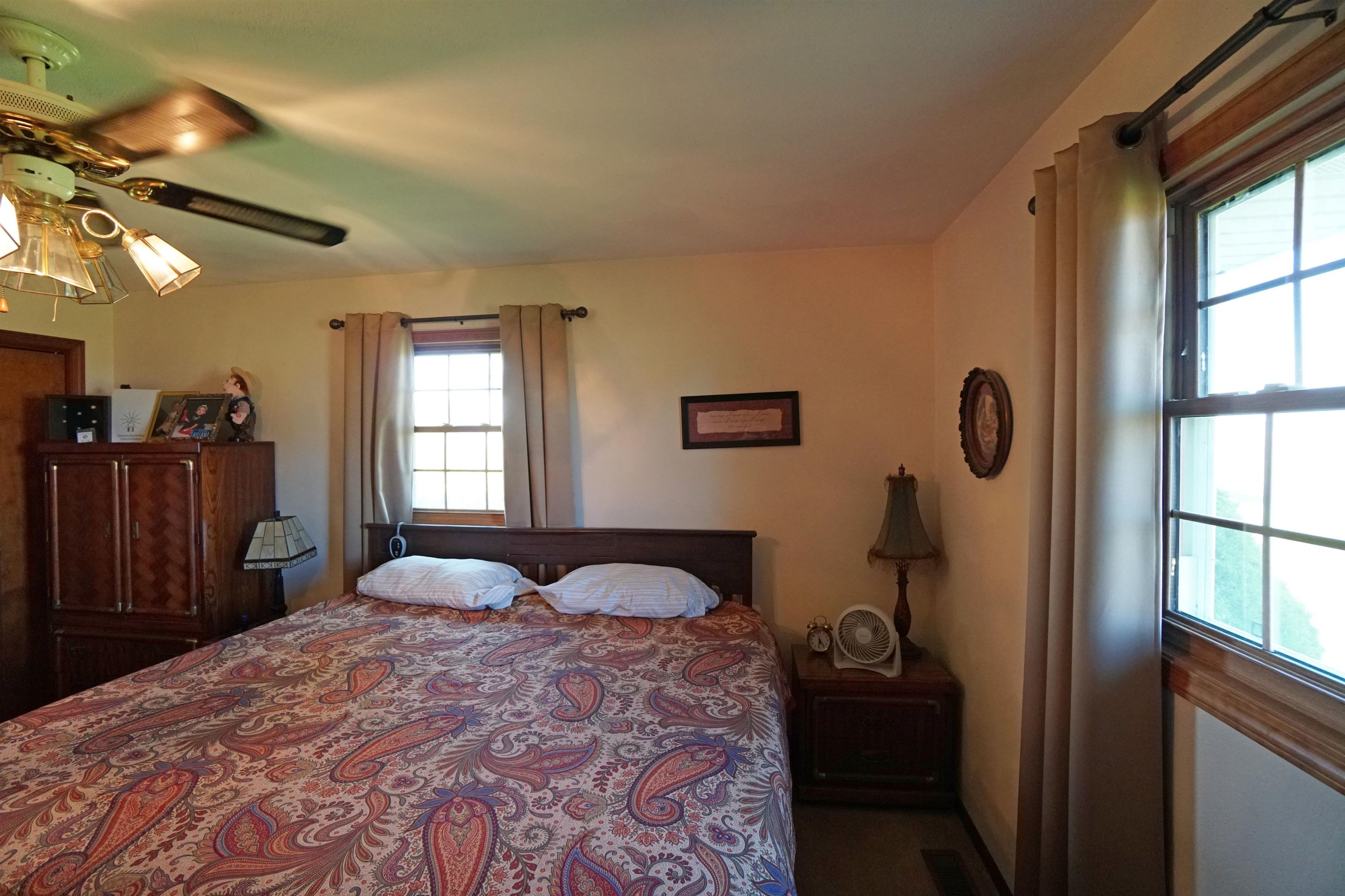 Furnished bedroom with a paisley bedspread, dark wood furniture, and two curtained windows.