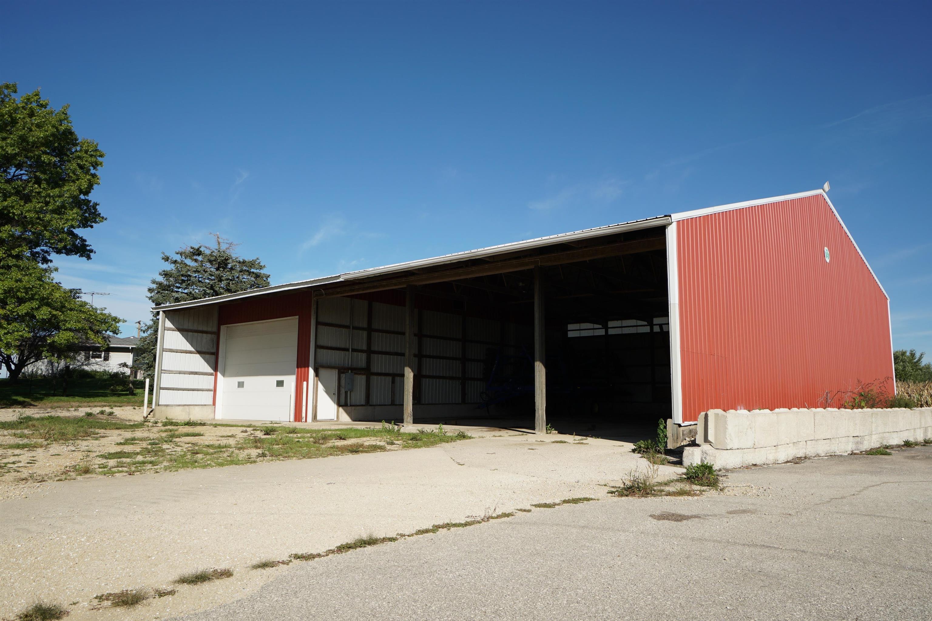 Red metal agricultural shed with a wide open bay and white garage door.