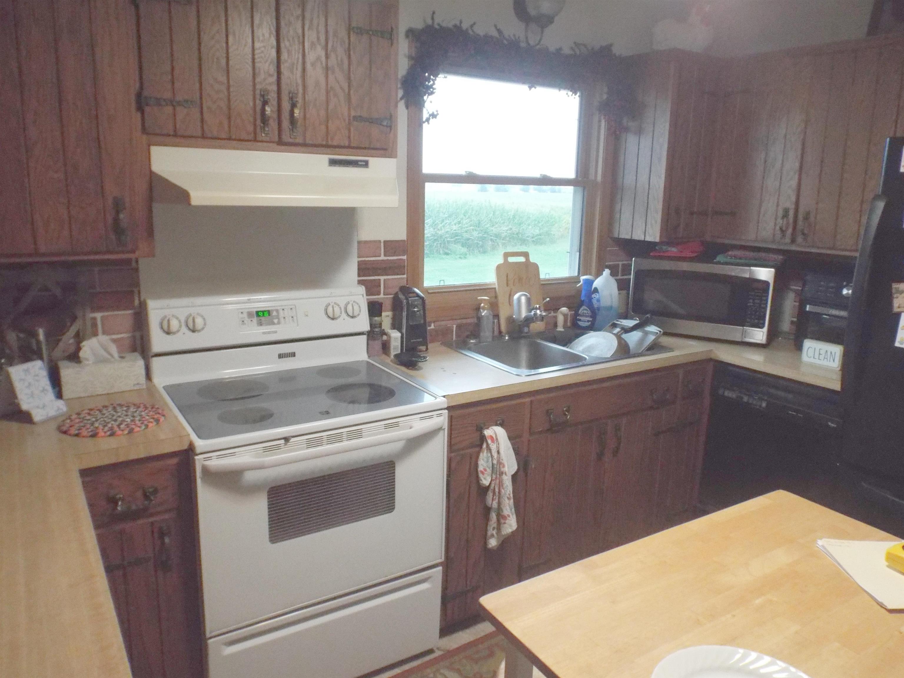 Kitchen with dark wood cabinets, white range, and sink beneath a window overlooking a field.