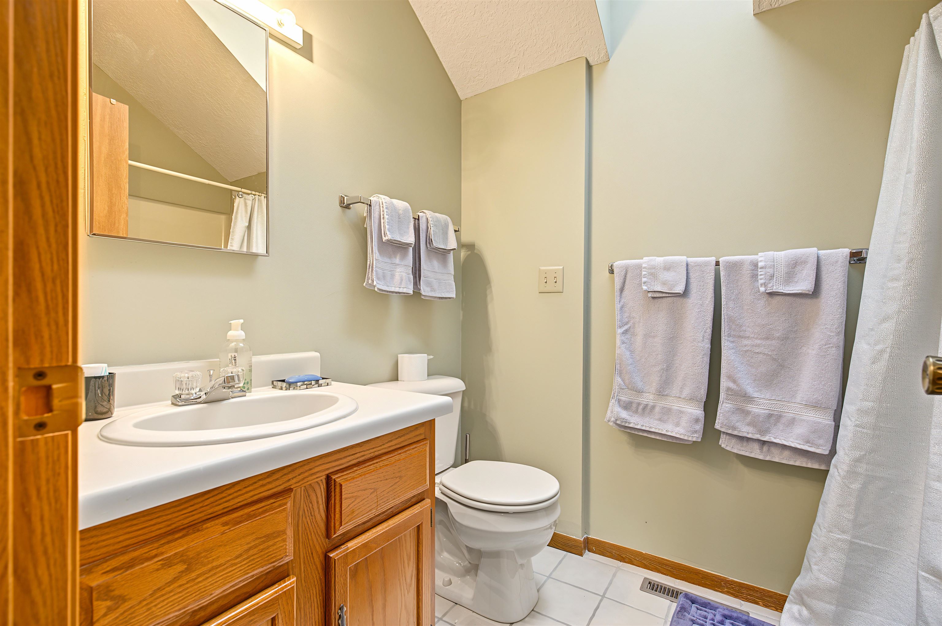 Bathroom with a wooden vanity, white sink, toilet, and neatly hung towels.