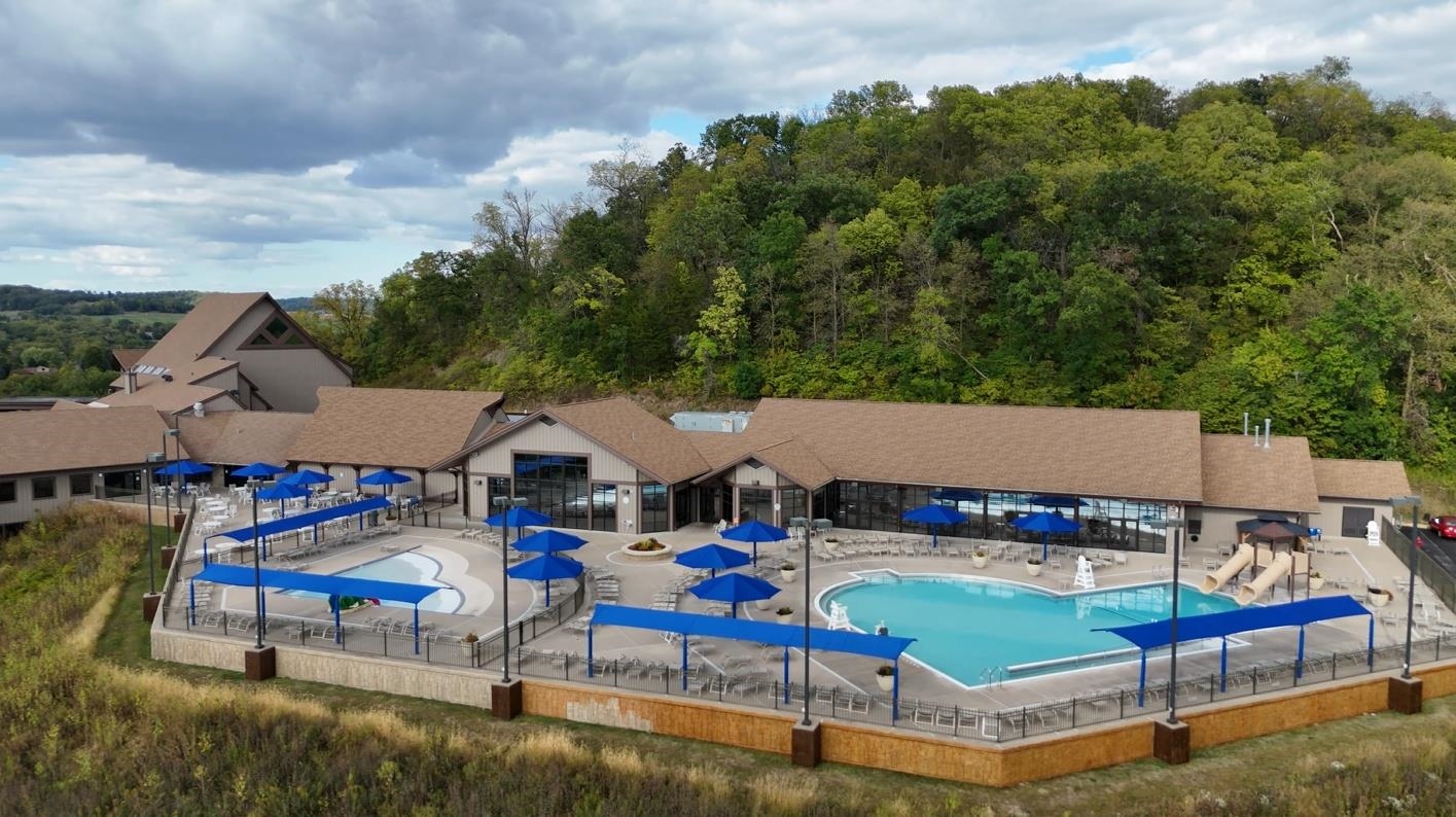 Aerial view of a clubhouse and outdoor pools with blue umbrellas and waterslides.