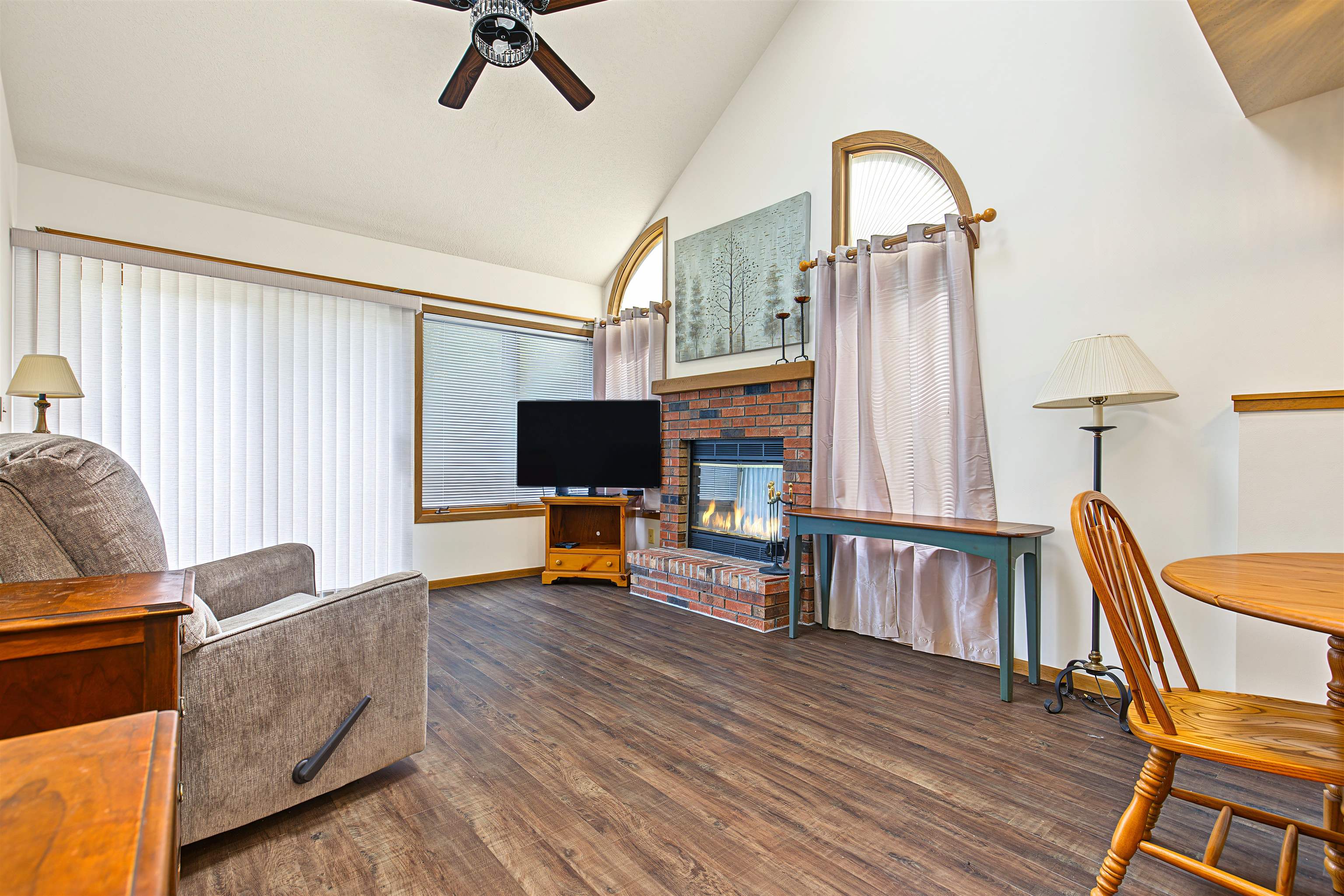 Living room with a brick fireplace, vaulted ceiling, and arched windows.