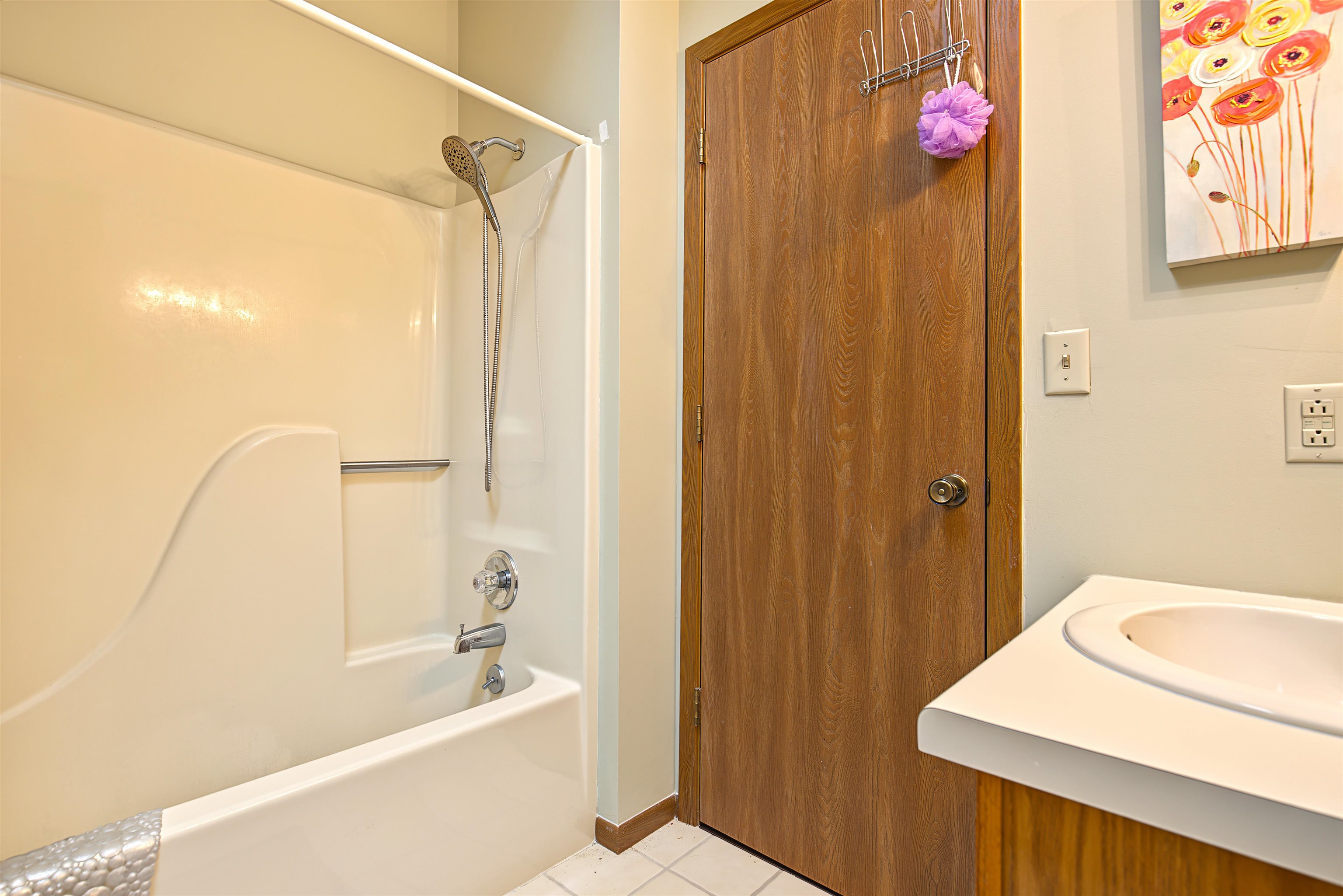 Bathroom with a white tub and shower beside a wood door and vanity sink.