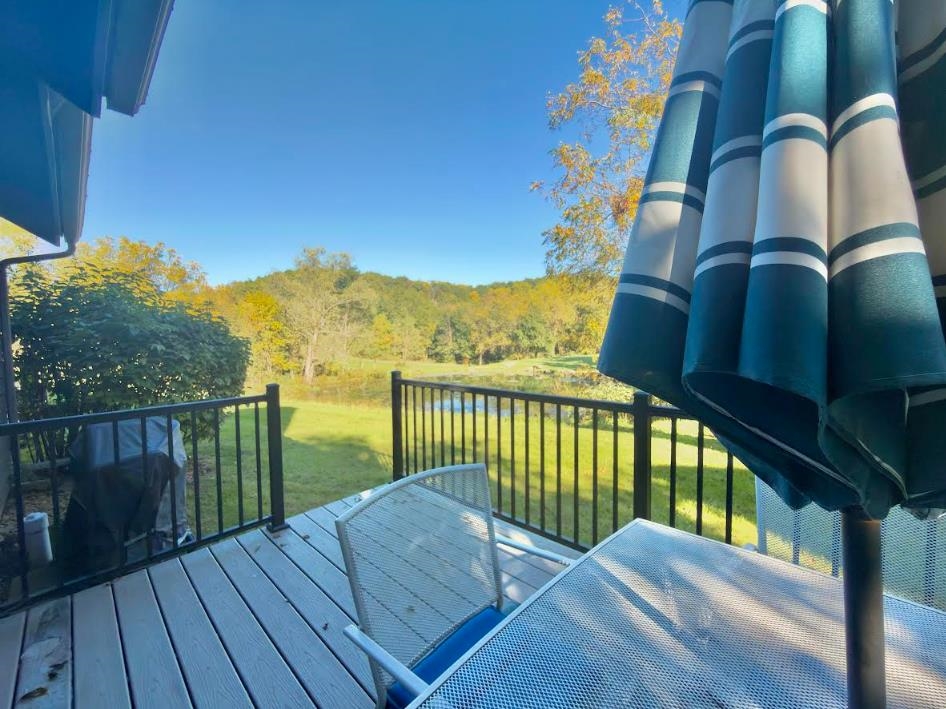 Deck with patio seating and striped umbrella overlooking a pond and autumn trees.