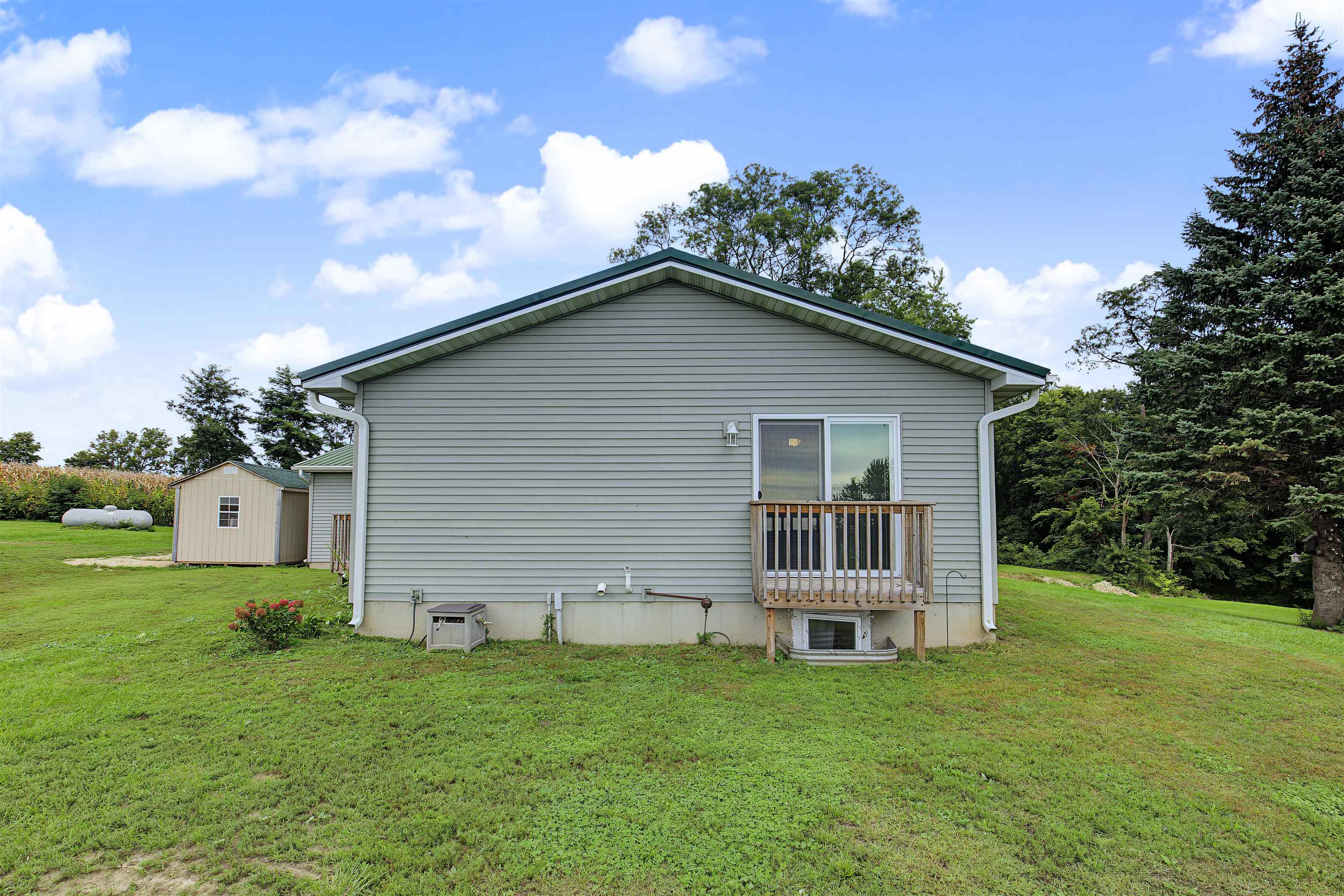 Rear of a gray-sided house with a small deck, grassy lawn, and detached shed.