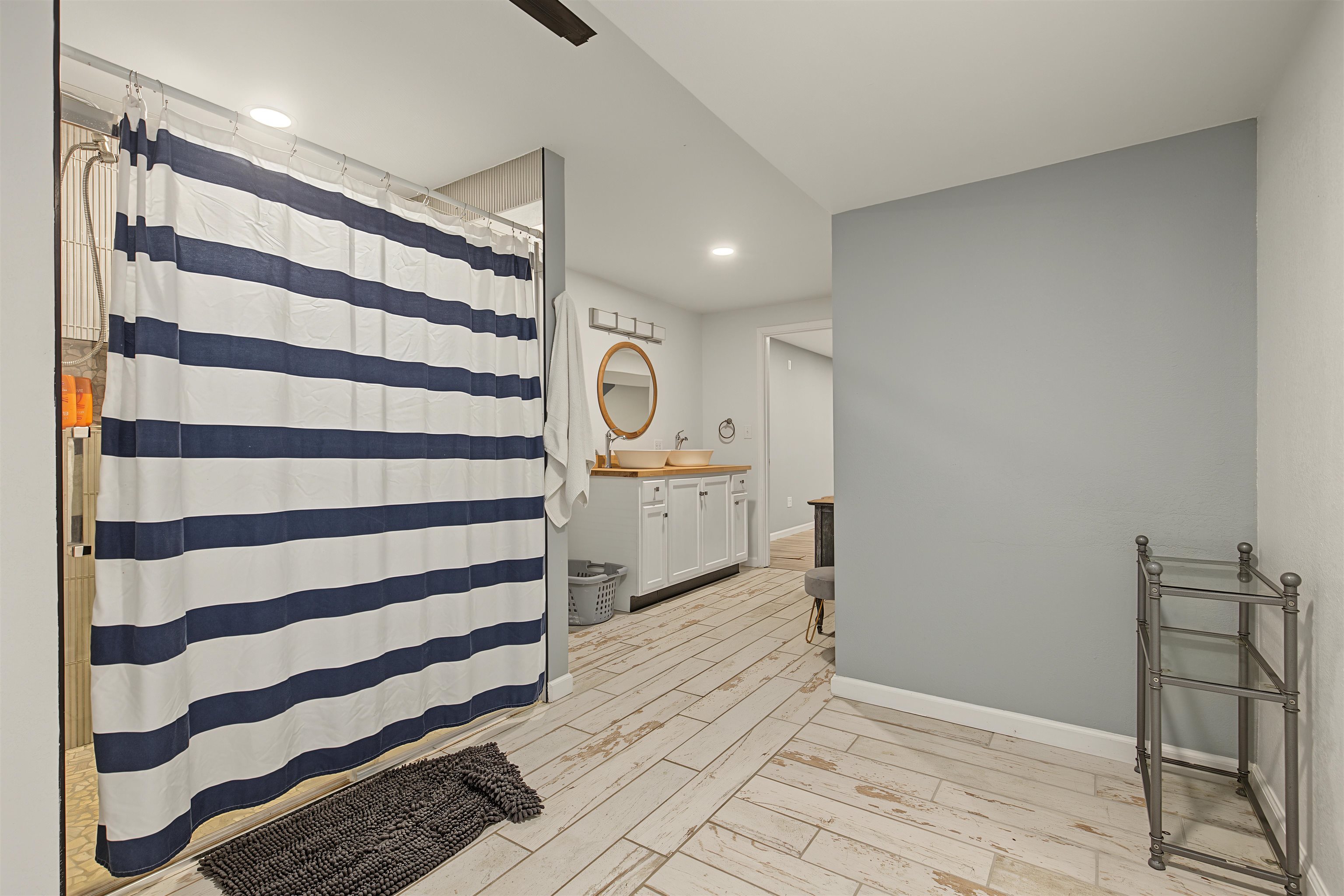Bathroom with a striped shower curtain, double vessel sinks, and distressed white plank flooring.