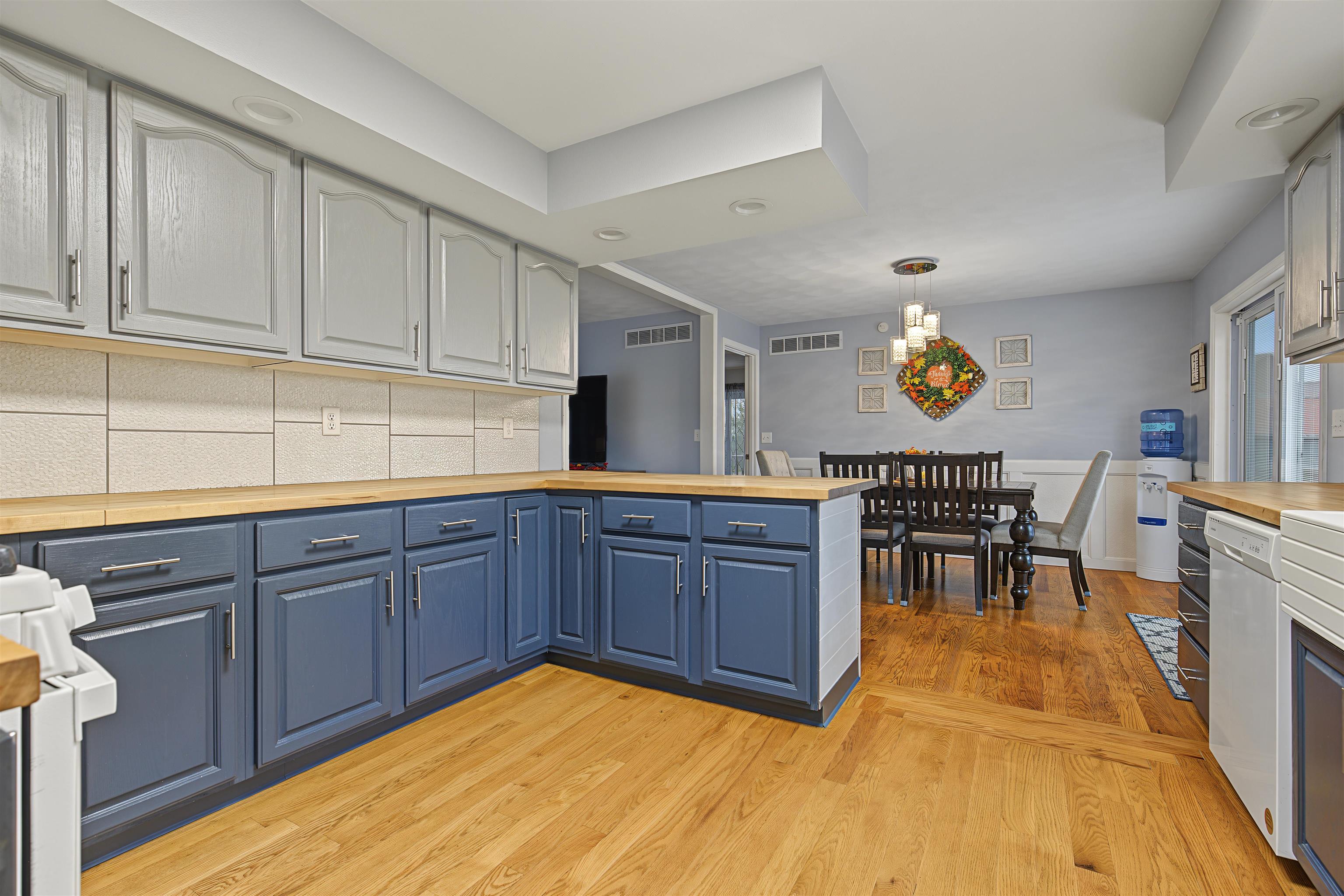Kitchen with blue lower cabinets, butcher-block counters, and a dining table on hardwood floors.
