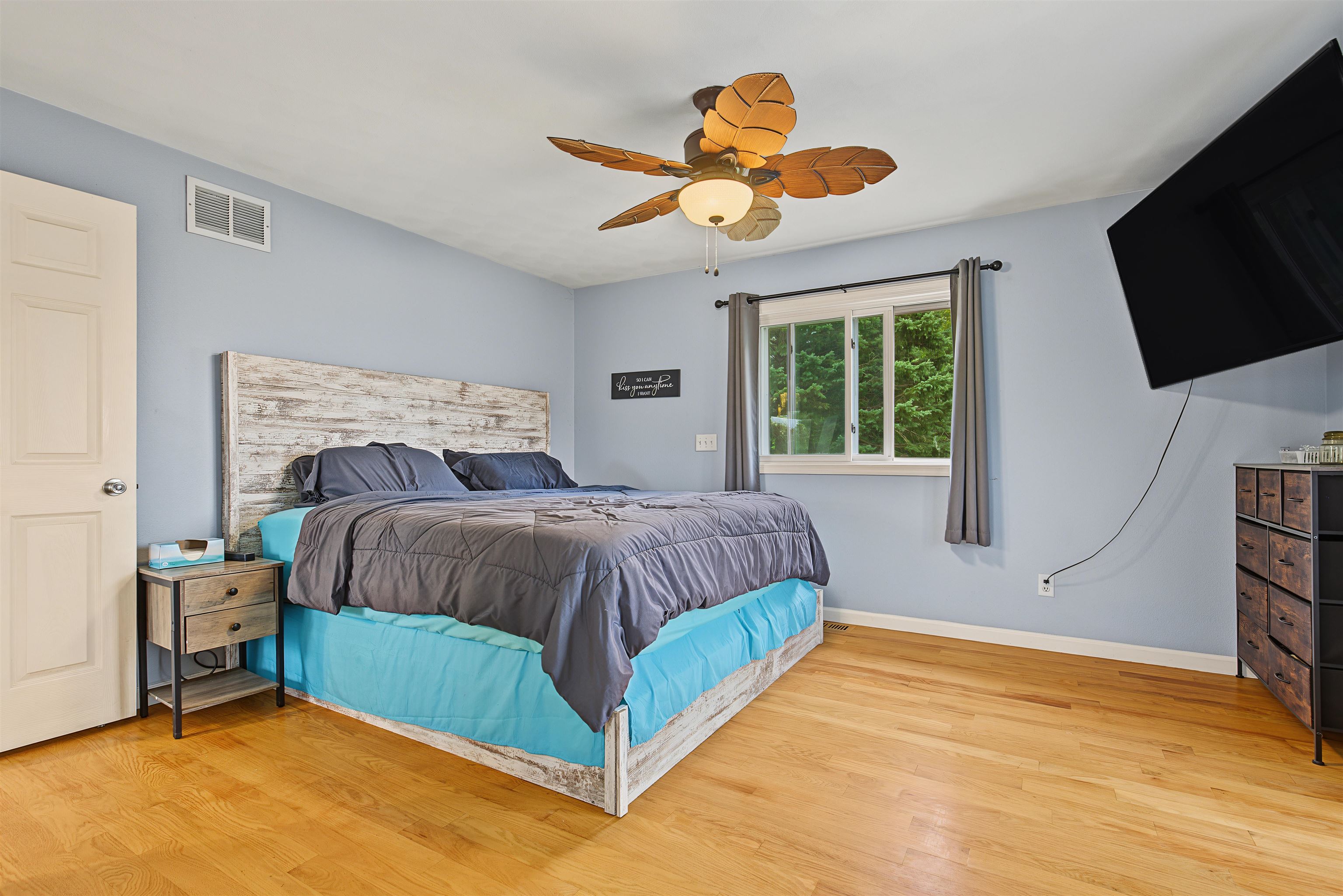 Bedroom with a large bed, turquoise bed skirt, hardwood floors, and a leaf-shaped ceiling fan.