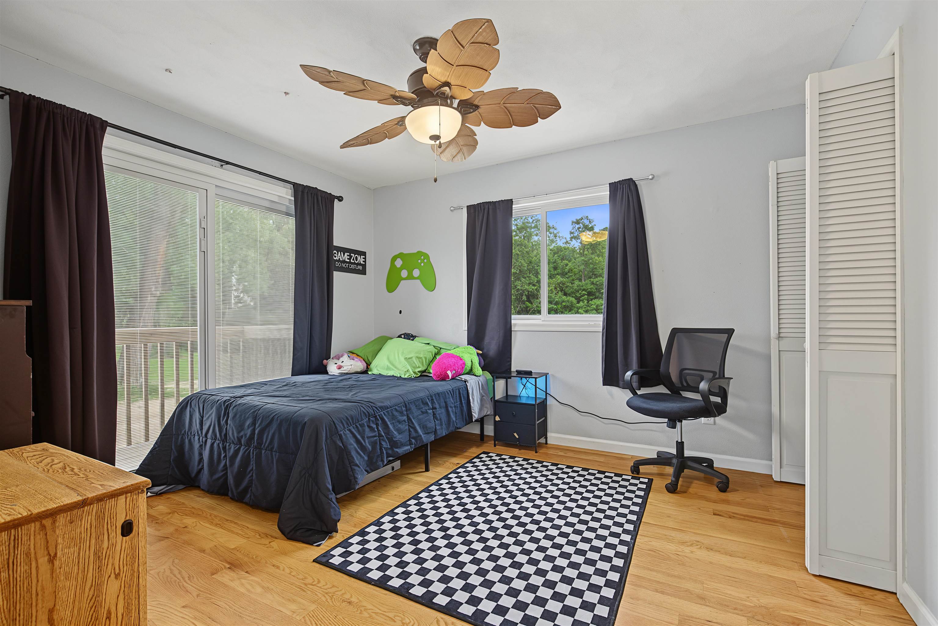 Bedroom with gaming-themed wall decor, a checkerboard rug, and windows overlooking trees.