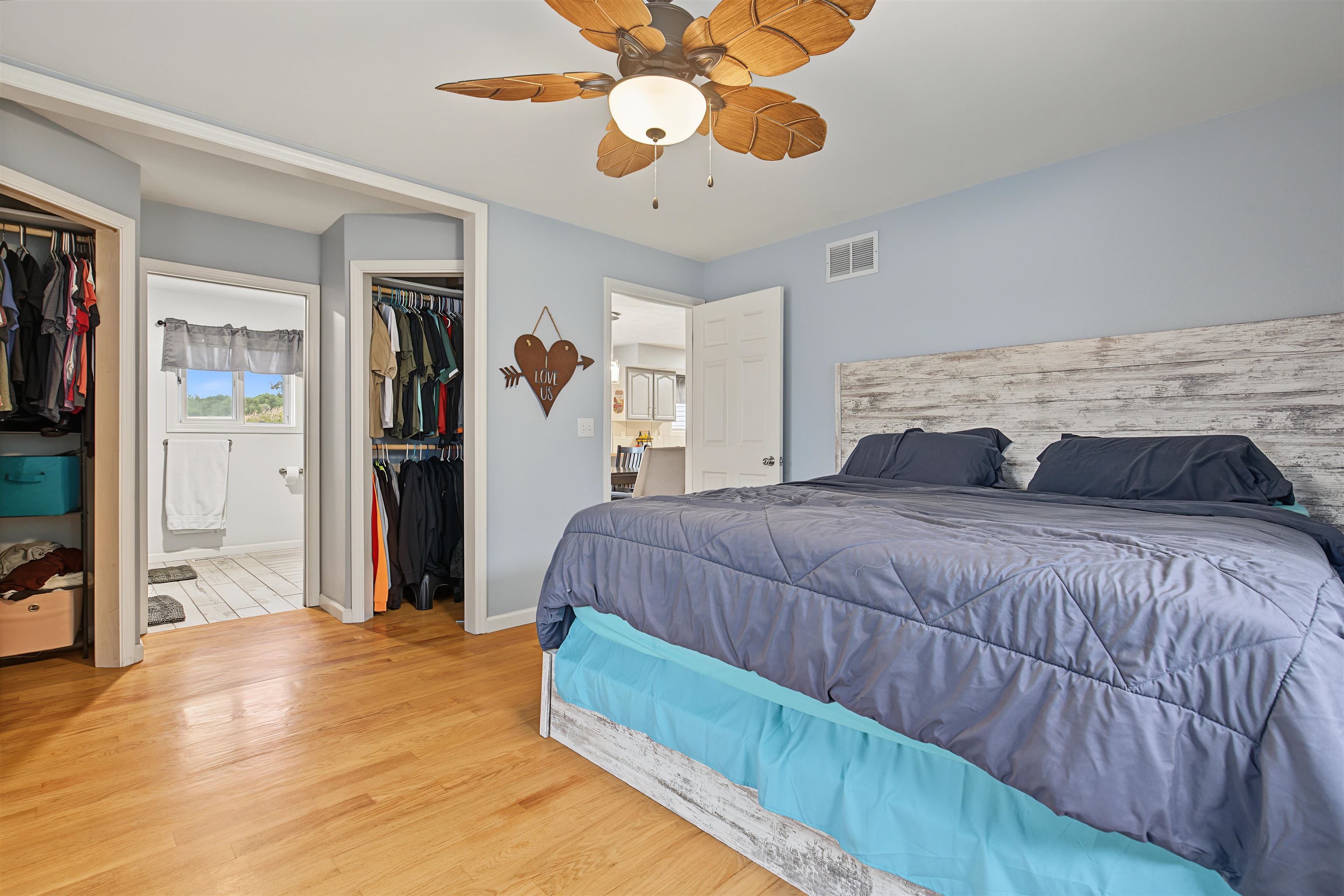 Bedroom with a large gray-and-turquoise bed, leaf-blade ceiling fan, and open closets.