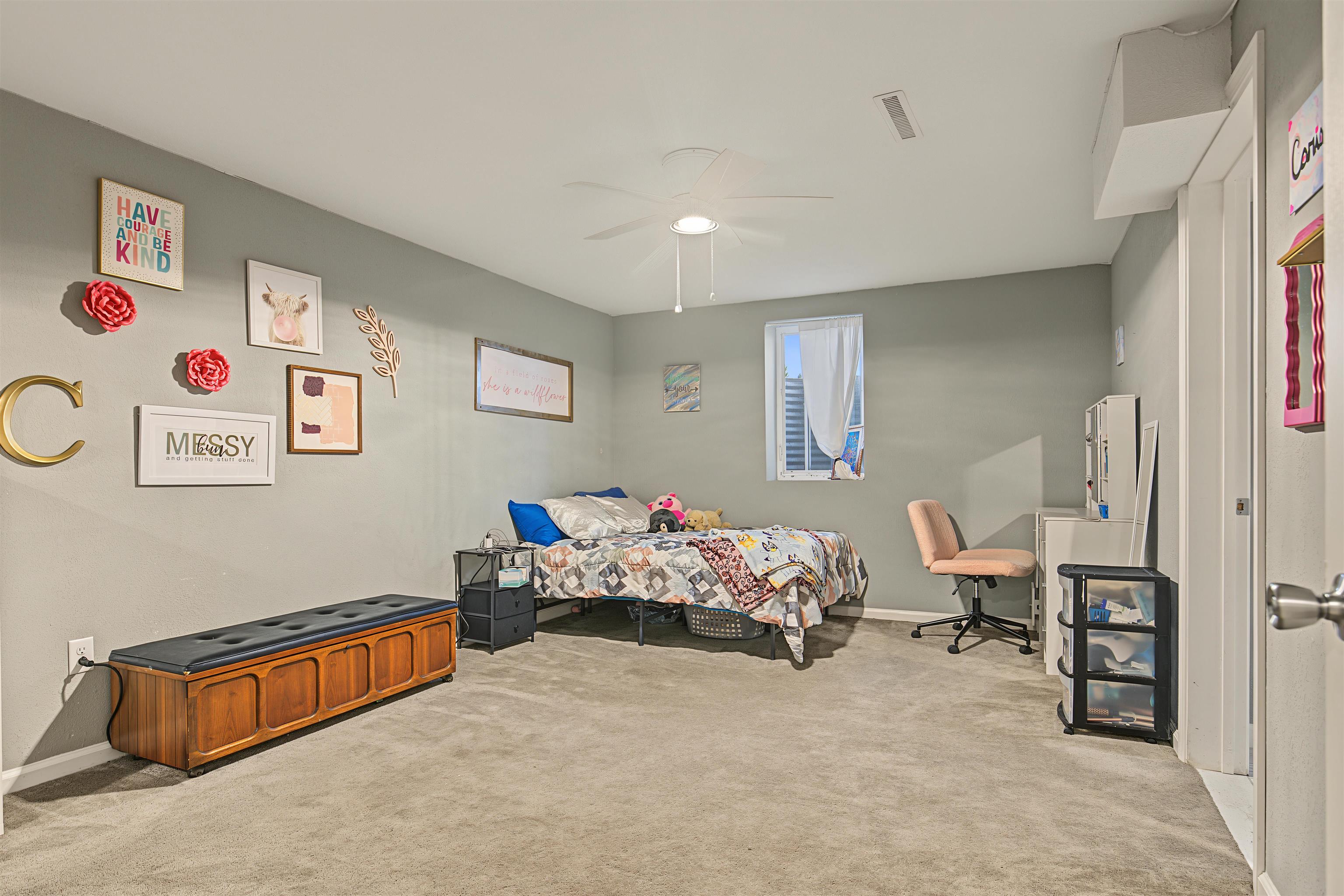 Furnished bedroom with a colorful bed, wooden storage bench, desk, and gray walls.