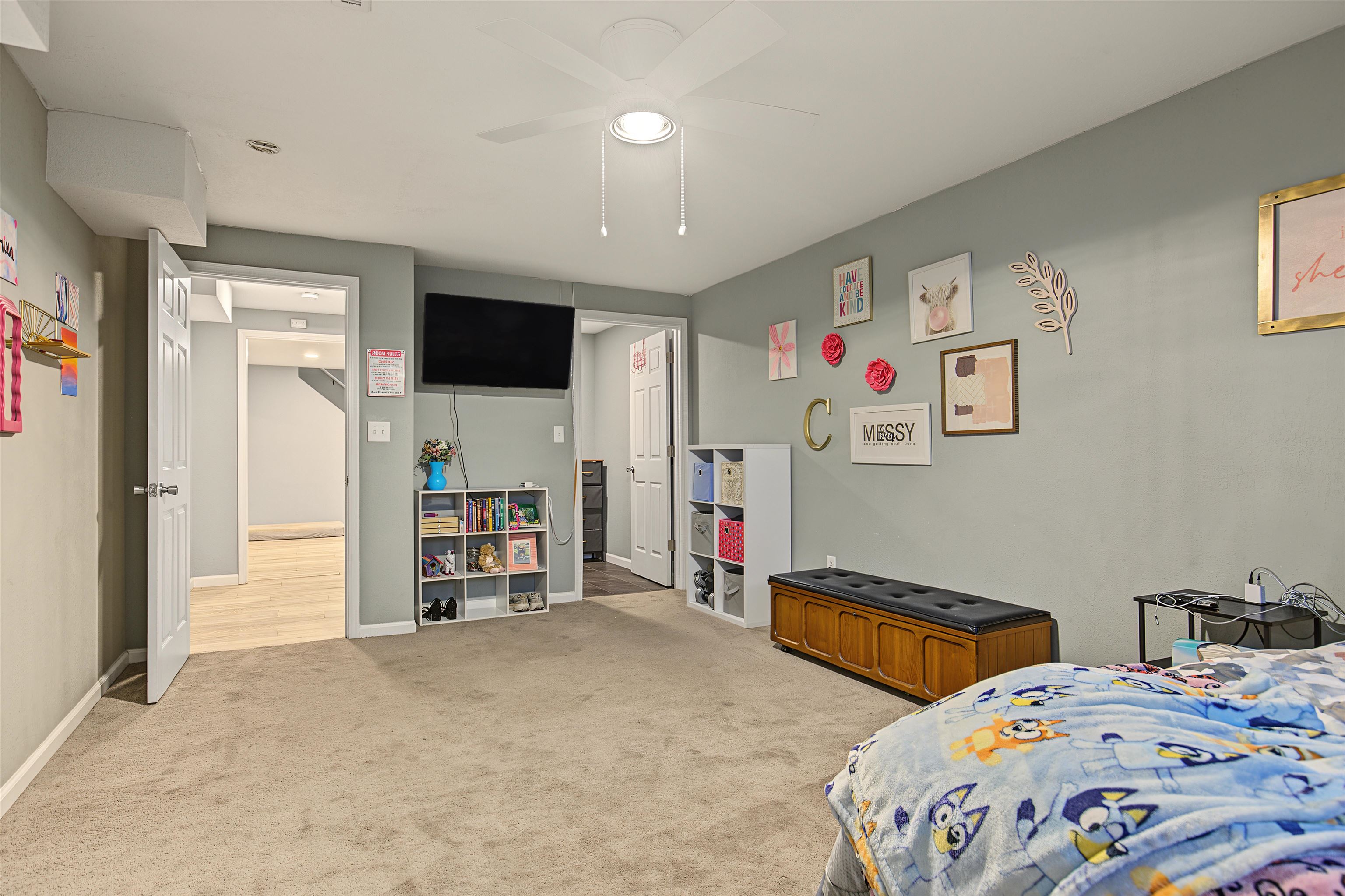 Bedroom with gray walls, a wall-mounted TV, cube shelves, and a colorful cartoon-print bedspread.